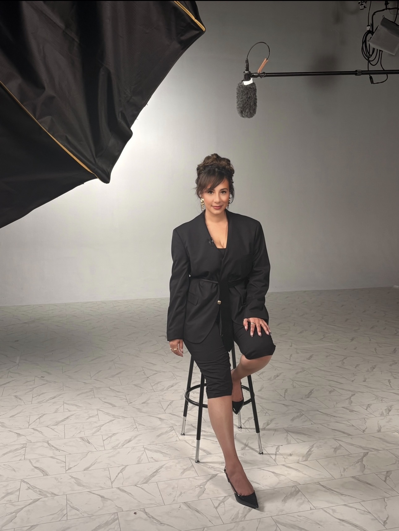 Woman sitting on a stool in a studio with professional lighting and microphone overhead.