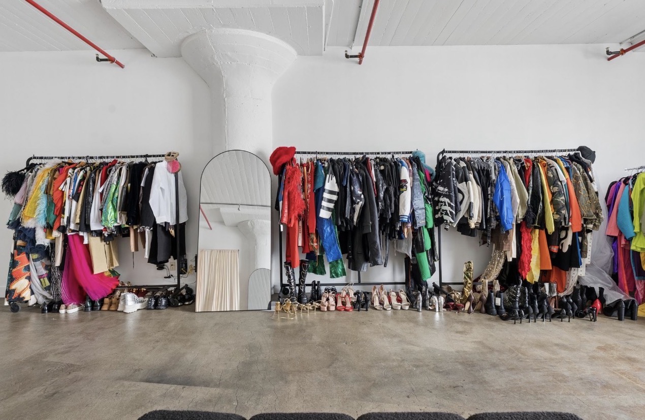 Three clothing racks filled with colorful clothes in a spacious room with white walls and ceiling.