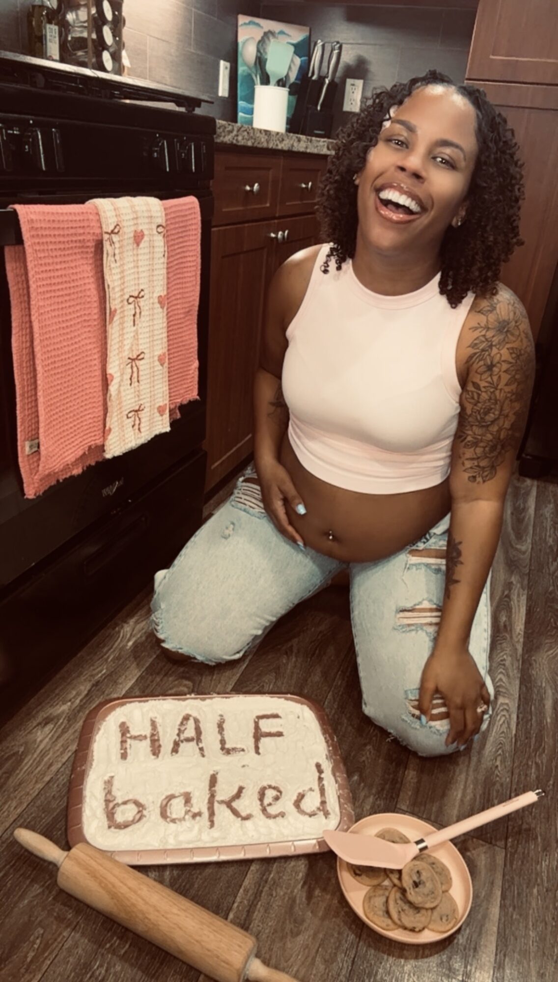 Woman kneeling on floor next to baked sign and bowl with spoon, smiling in kitchen.
