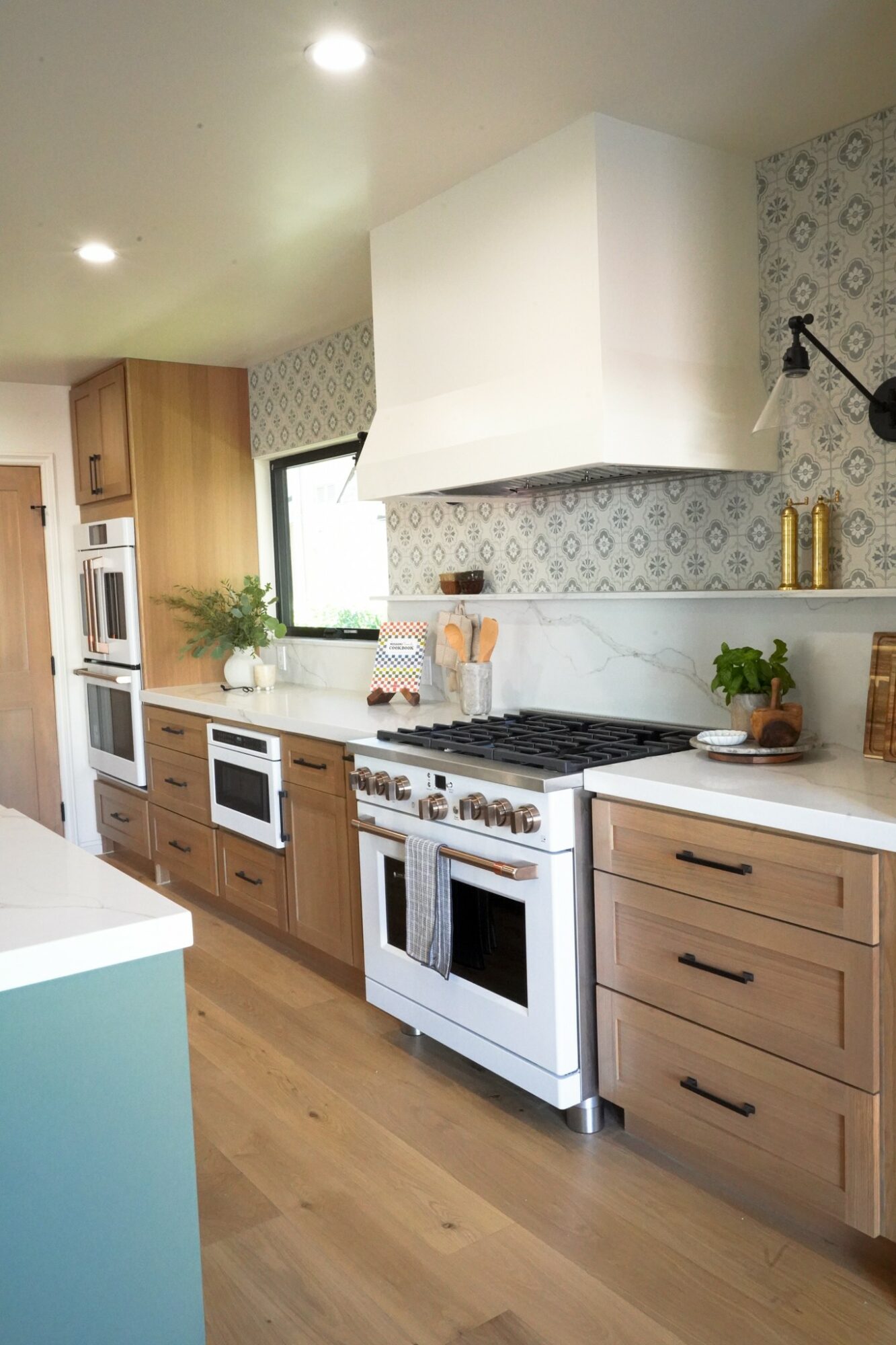 Kitchen with white stove, wooden cabinets, patterned wallpaper, and a window with a plant on the counter.