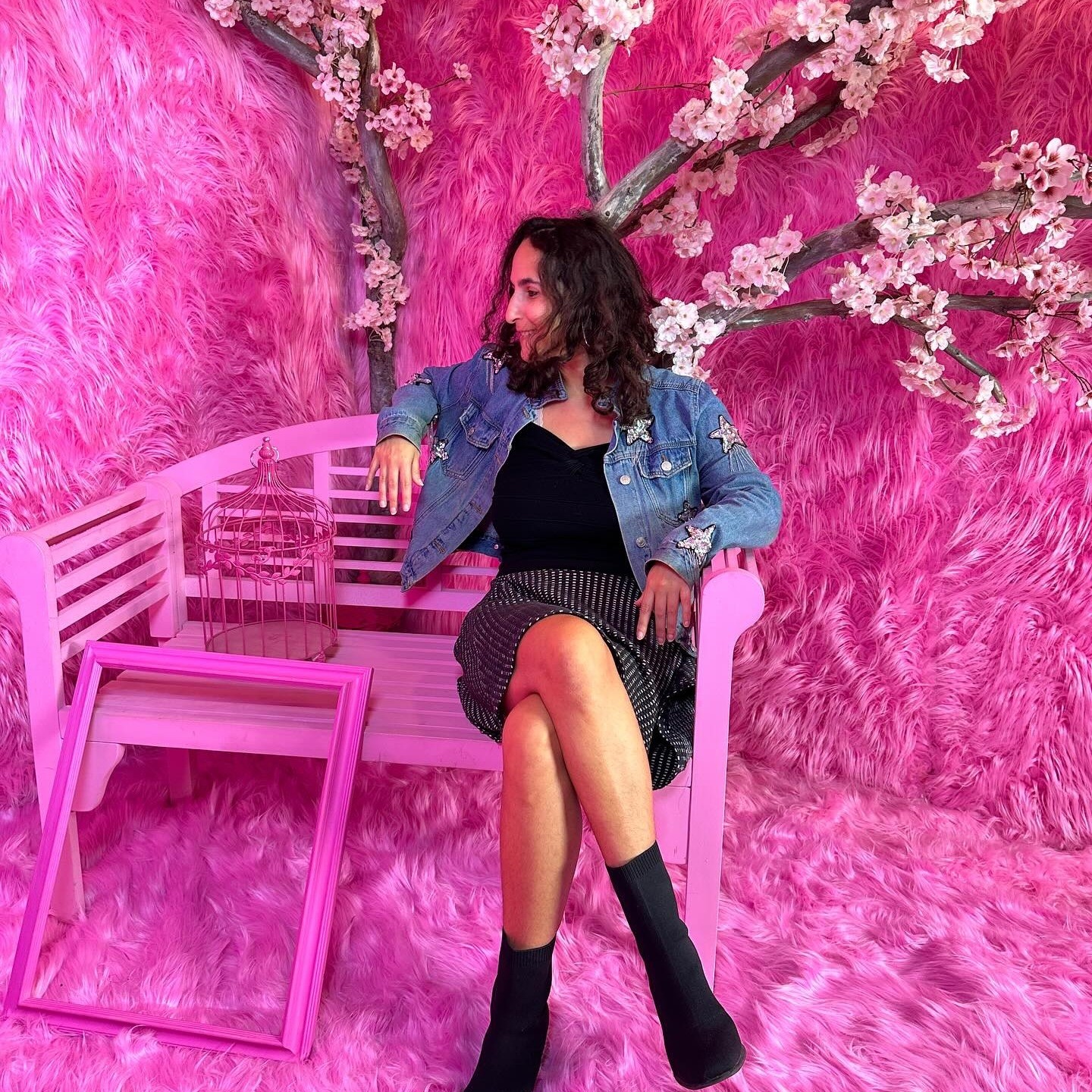 Woman sitting on pink bench with pink furry background and cherry blossom tree behind her.