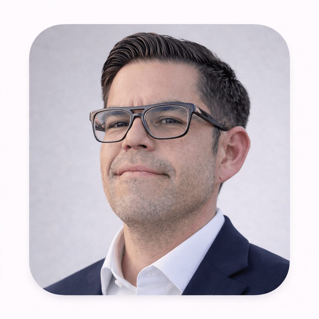 Man with glasses in a suit and white shirt against a plain background.