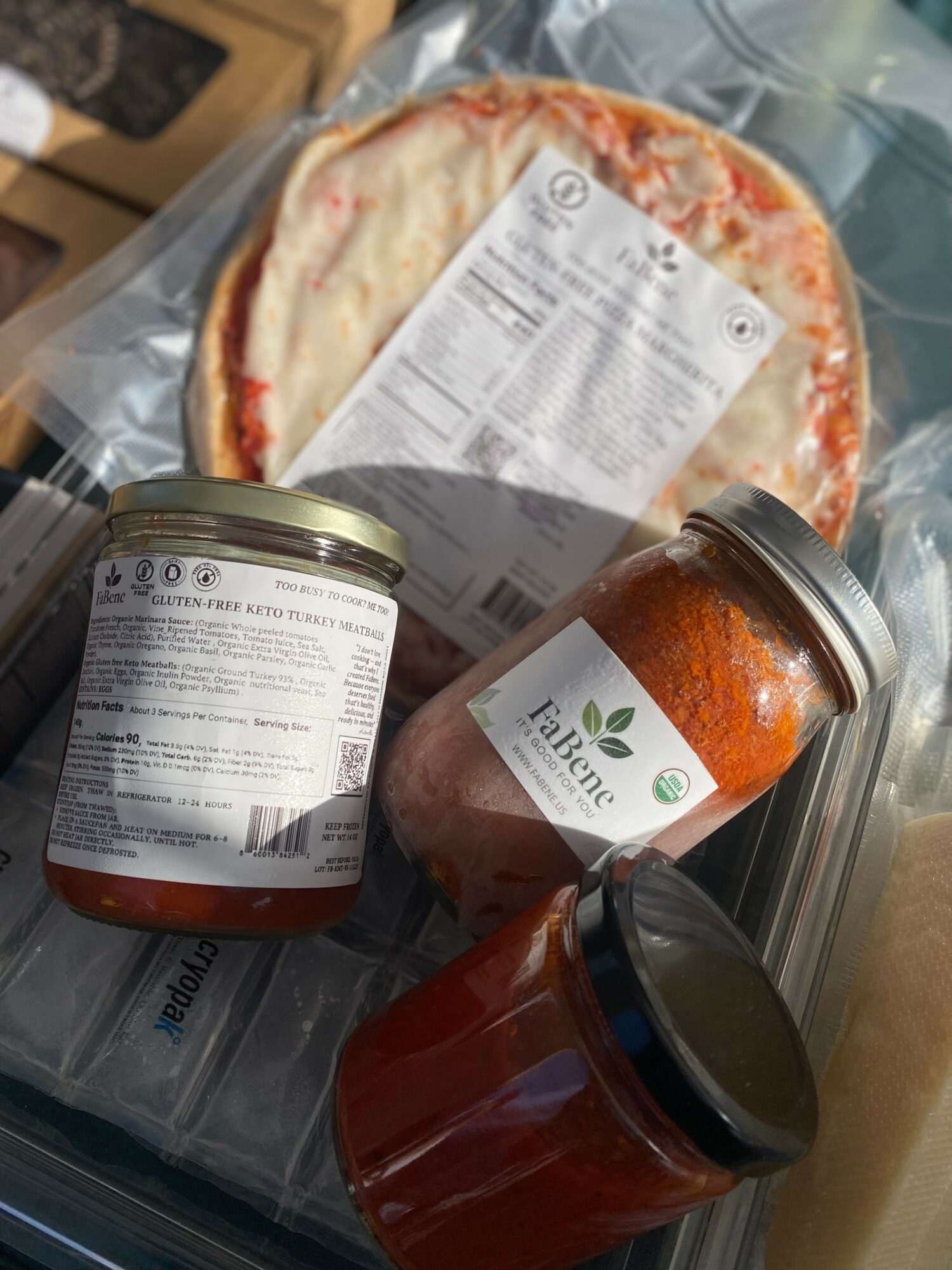 Frozen pizza, two jars of sauce, and a container of cheese on a plastic surface.