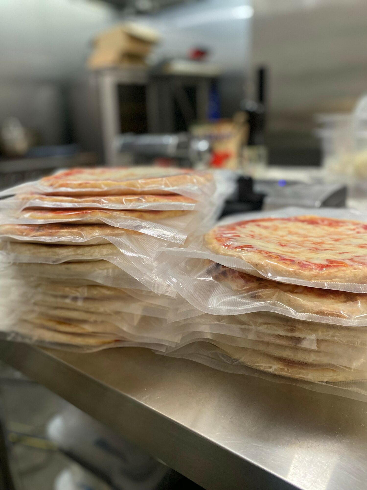 Stacks of frozen pizza in plastic wrap on a kitchen counter with blurred background.