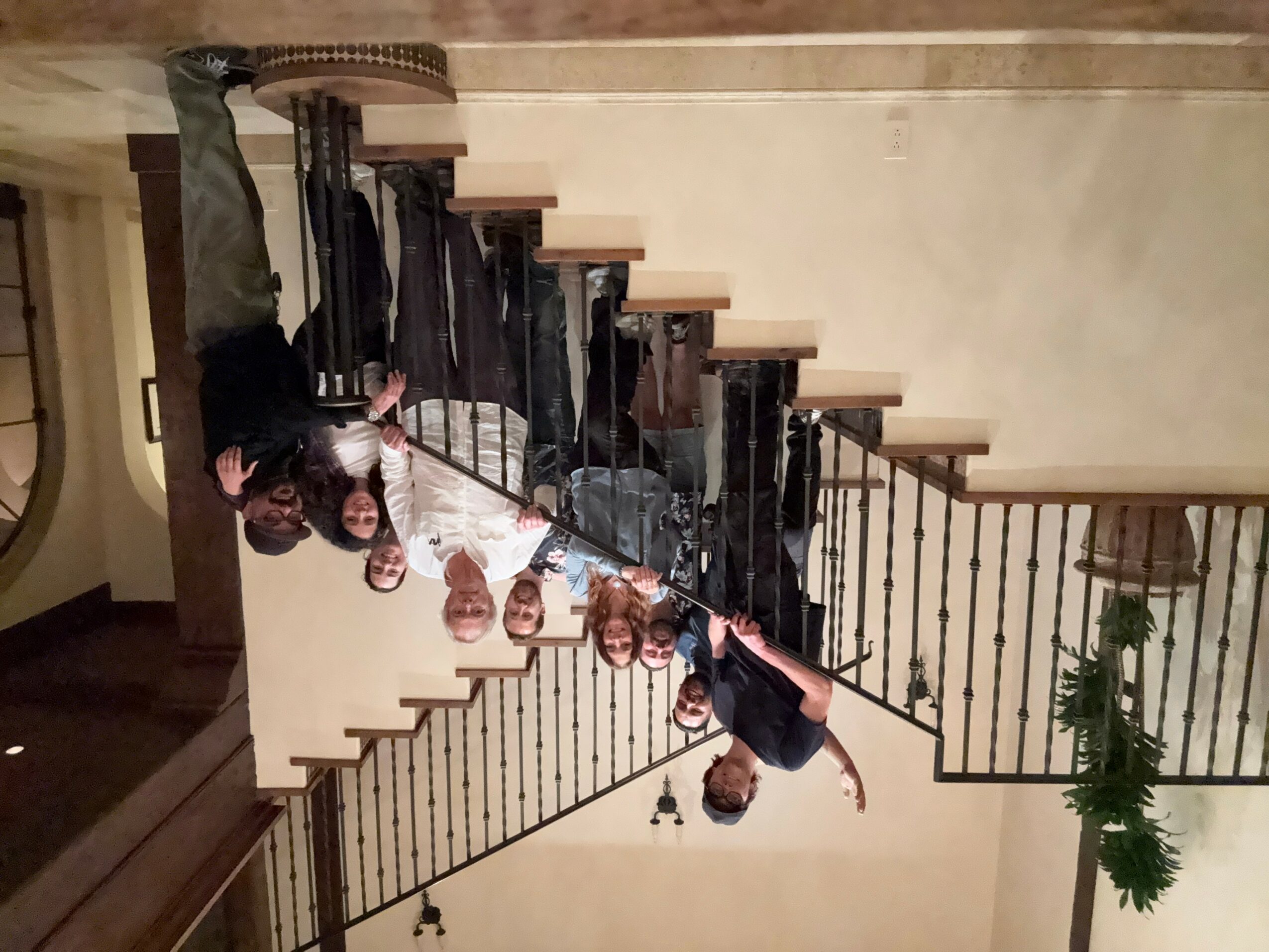 Group of people standing on staircase, some holding a long stick or pole, in an indoor setting with a railing and wall.