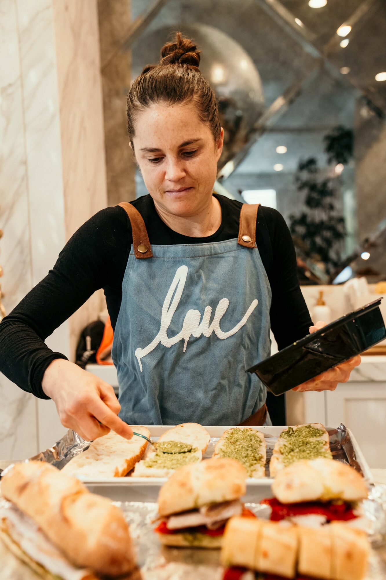 Young woman in apron preparing sandwiches at a counter in a cafe or bakery.