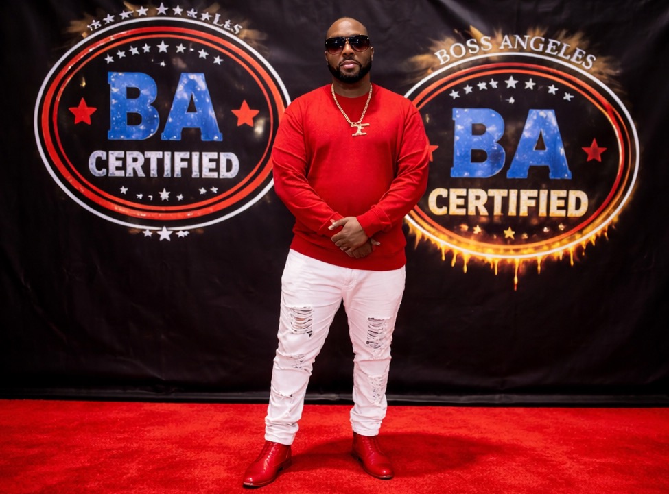 Man in red shirt and white pants standing on red carpet in front of BA Certified signs.