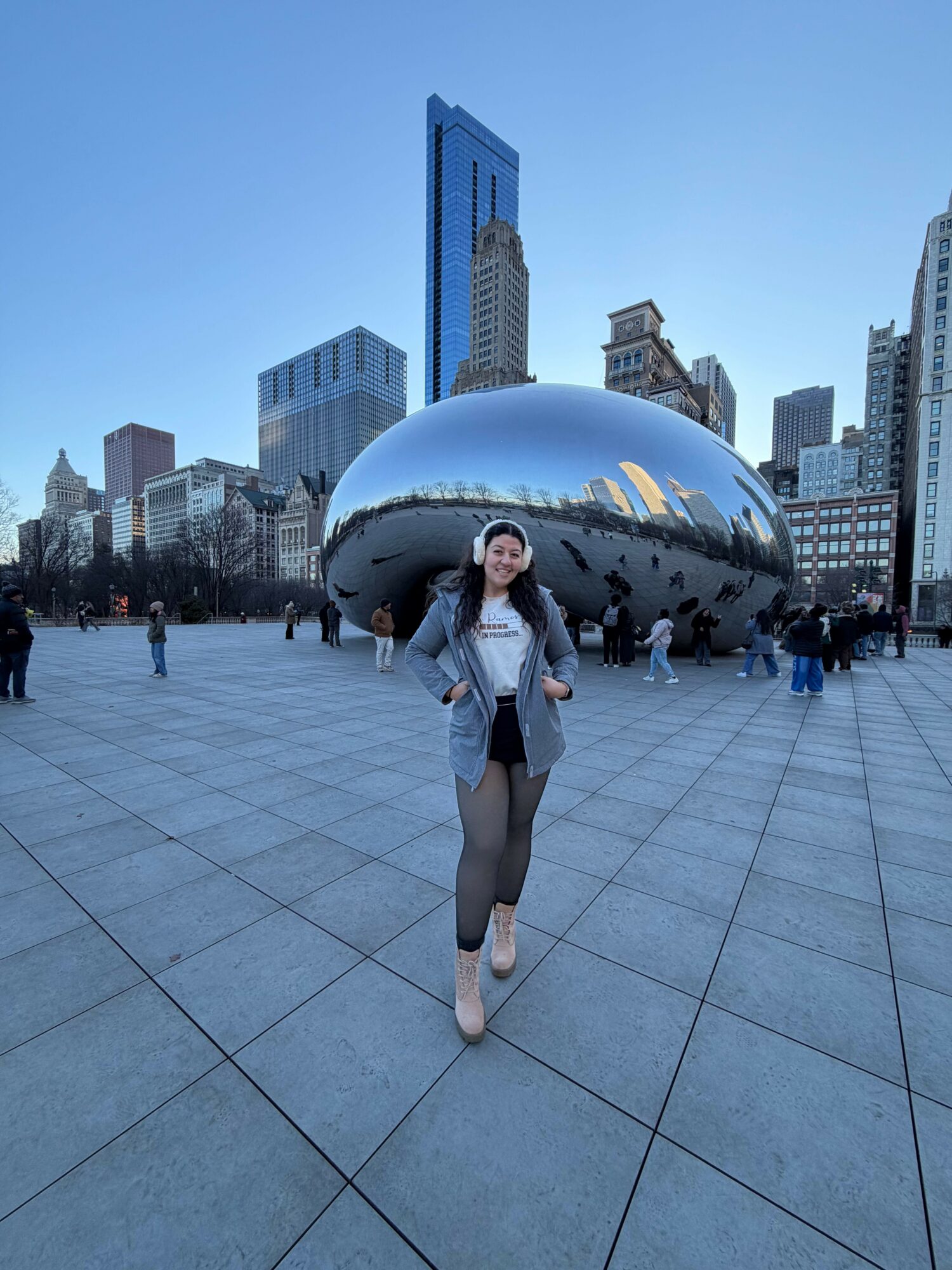 Woman standing in front of Cloud Gate sculpture in Millennium Park, Chicago, with city skyline behind.