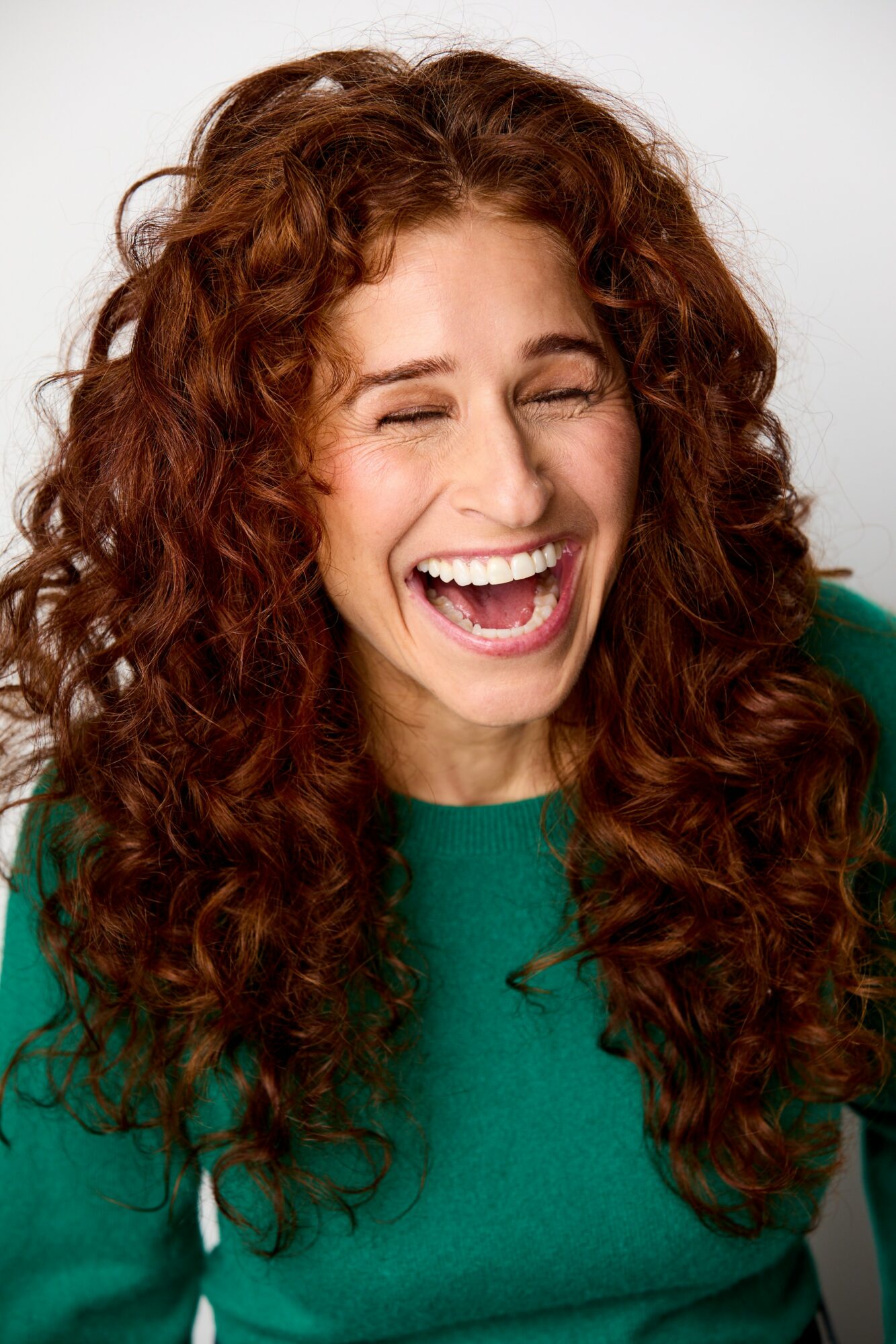 Woman with curly hair laughing and smiling, wearing a green top.