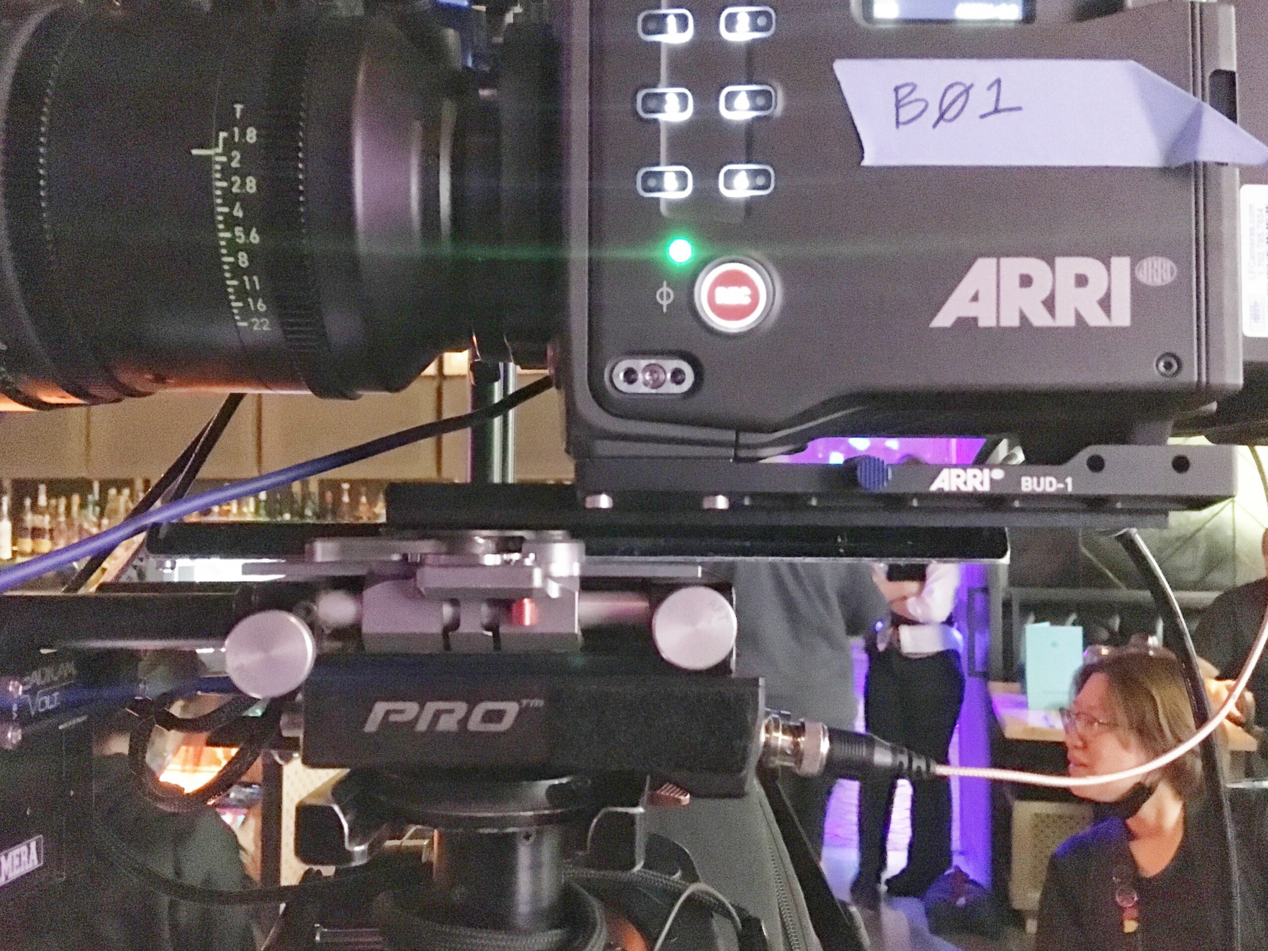 Camera setup with ARRI device and monitor, labeled B01, in a studio with people in the background.