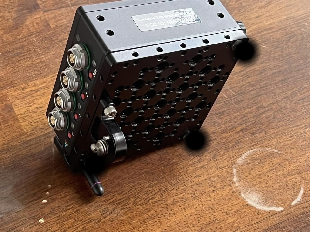 Black electronic device with multiple ports on the side, placed on a wooden surface with a circular mark nearby.