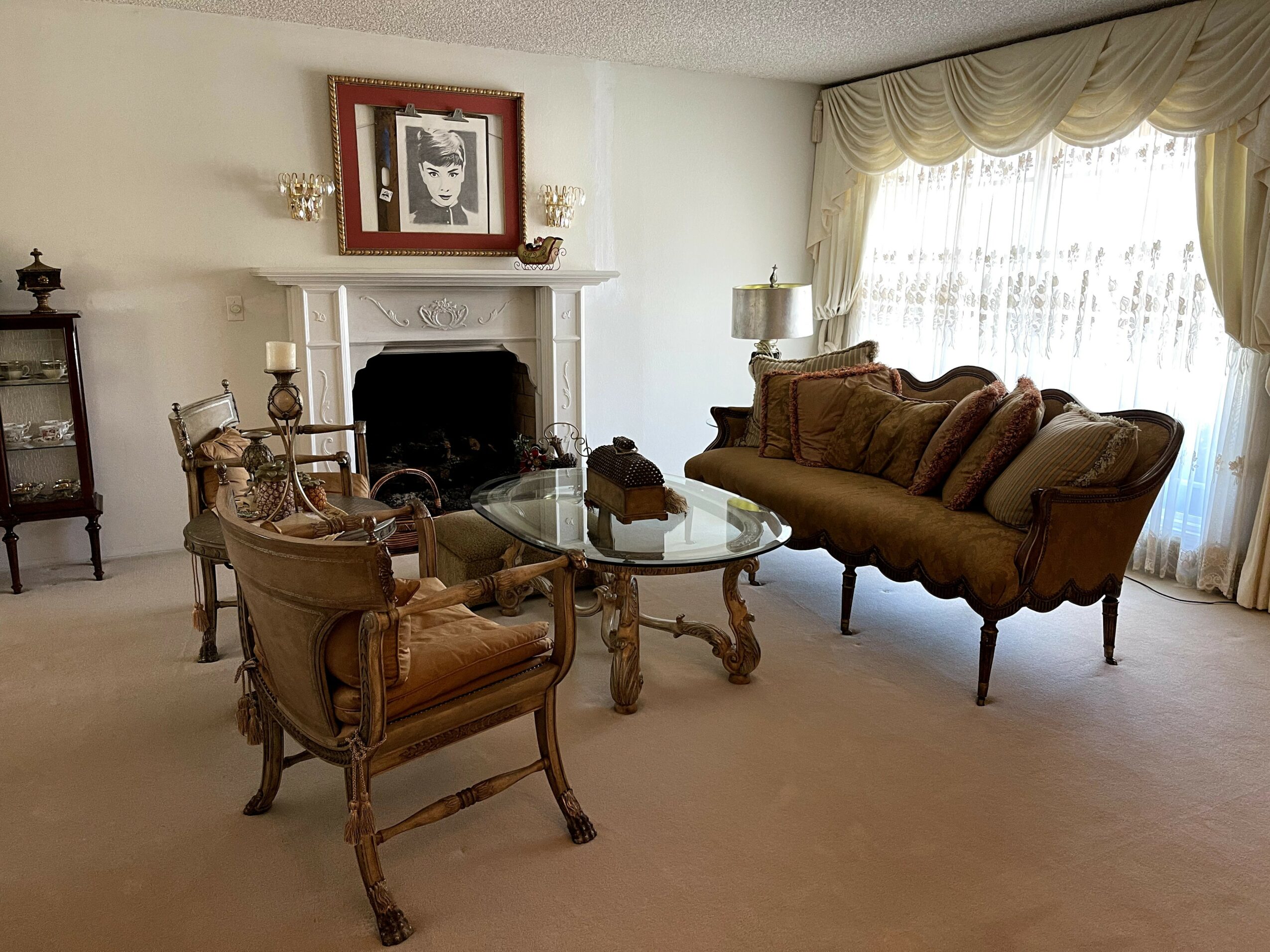 Living room with a fireplace, glass table, armchair, sofa, and window with curtains.