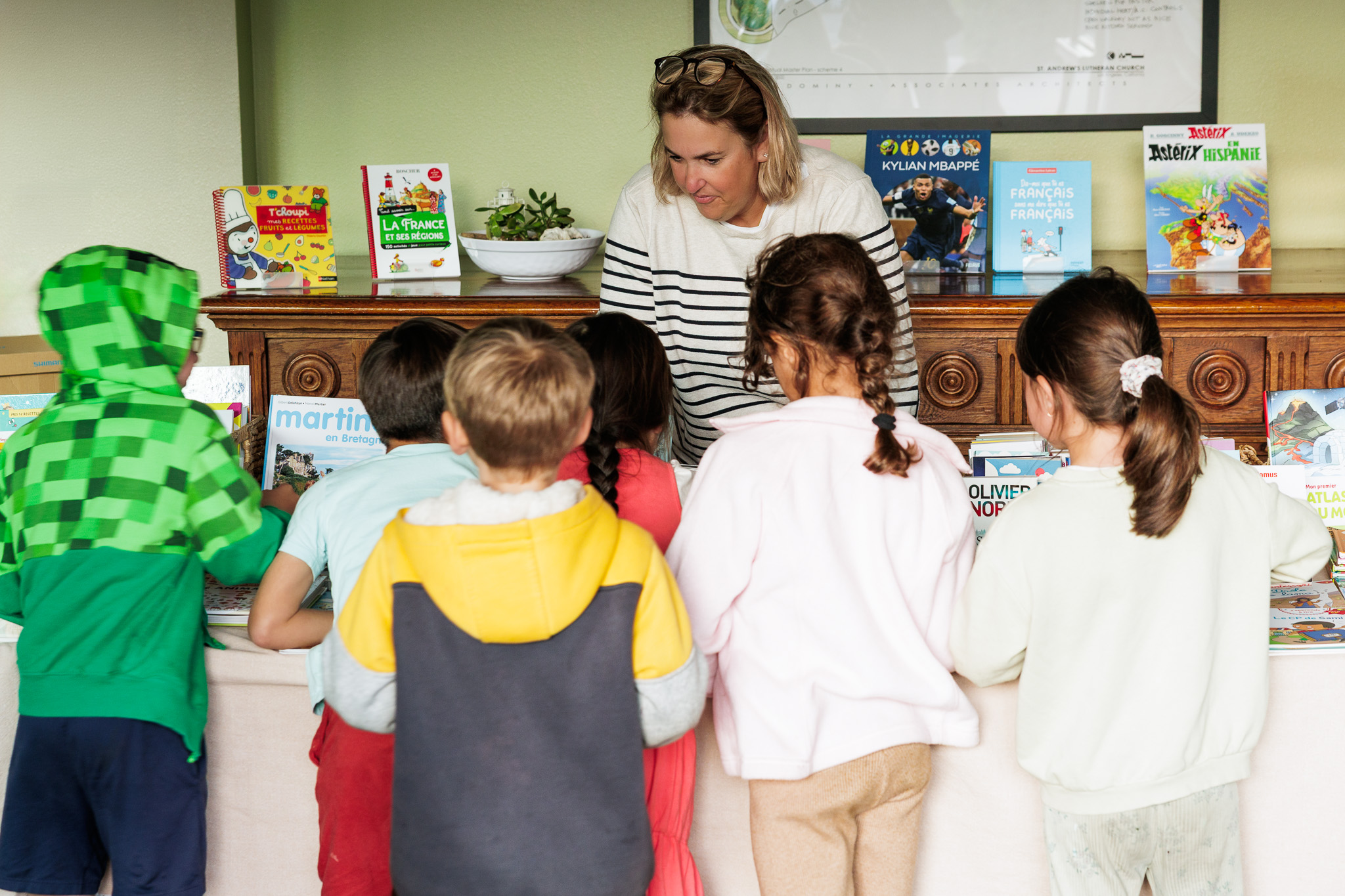 Woman reading to children in a classroom with books on a shelf behind her.