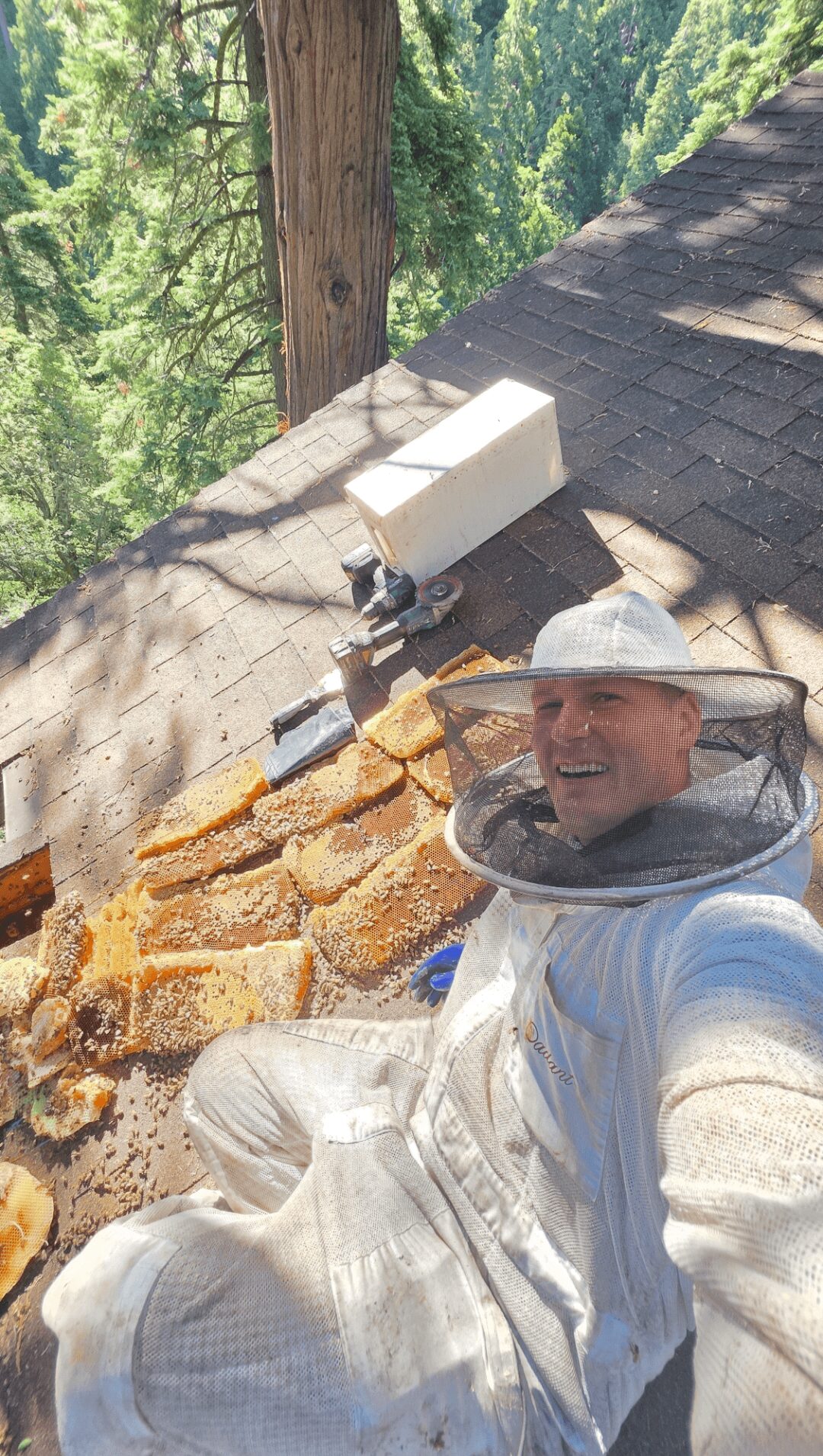 Person in protective suit taking a selfie outdoors with bread and a speaker on a wooden surface.