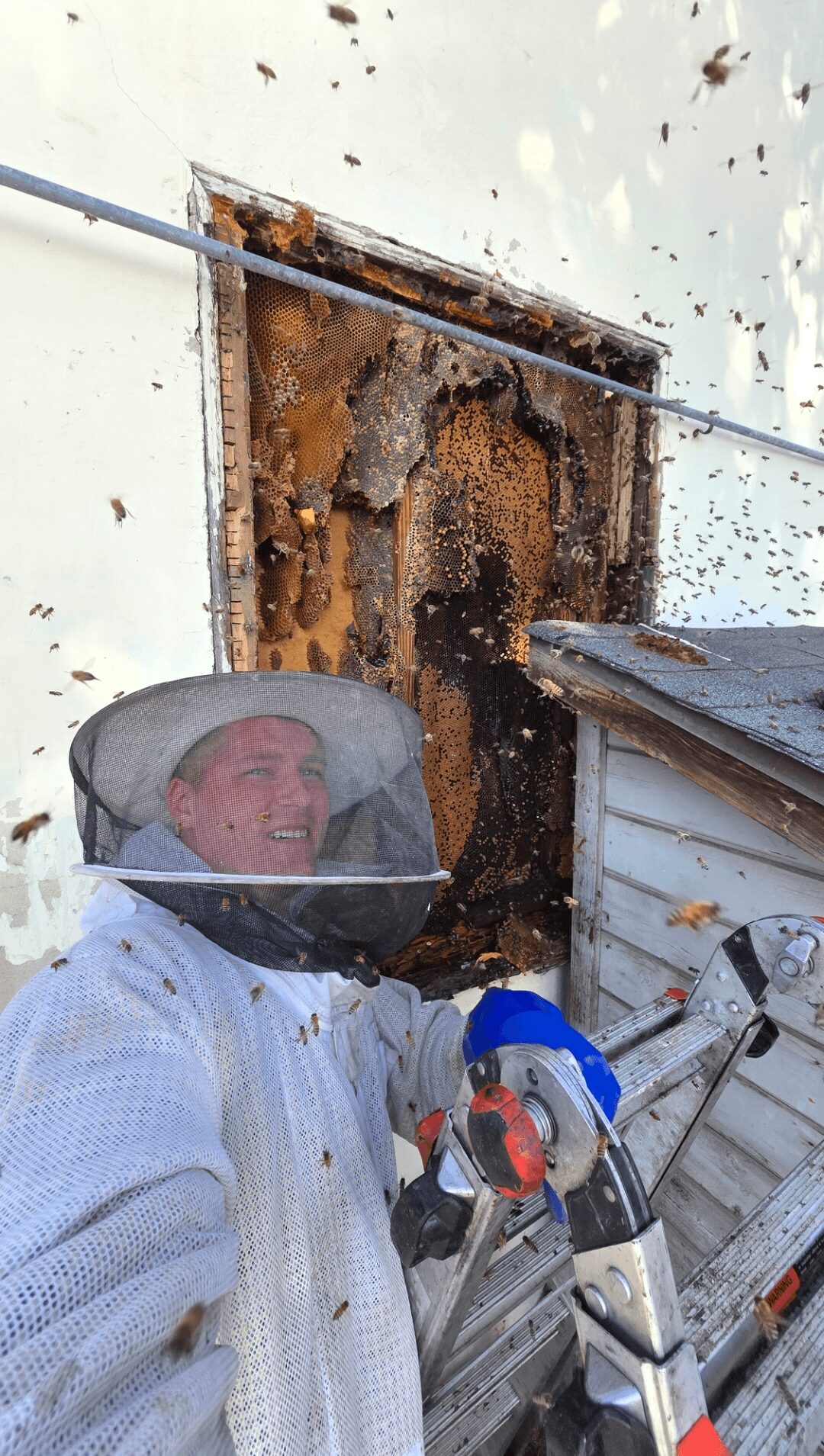 Person wearing protective gear holding a tool near a rusted, damaged wall opening.