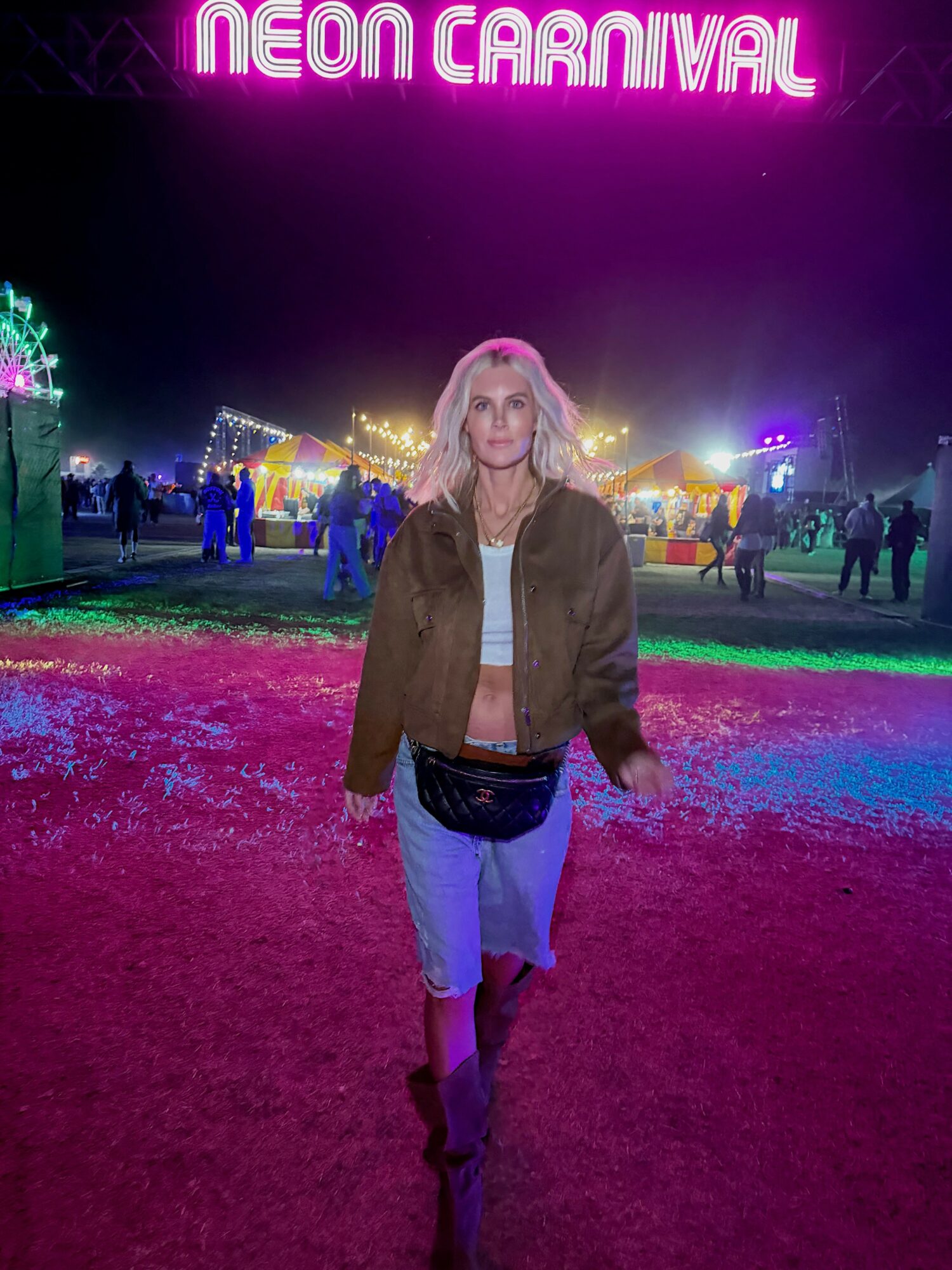 Woman standing on colorful ground at night with neon sign reading 'Neon Carnival' above.