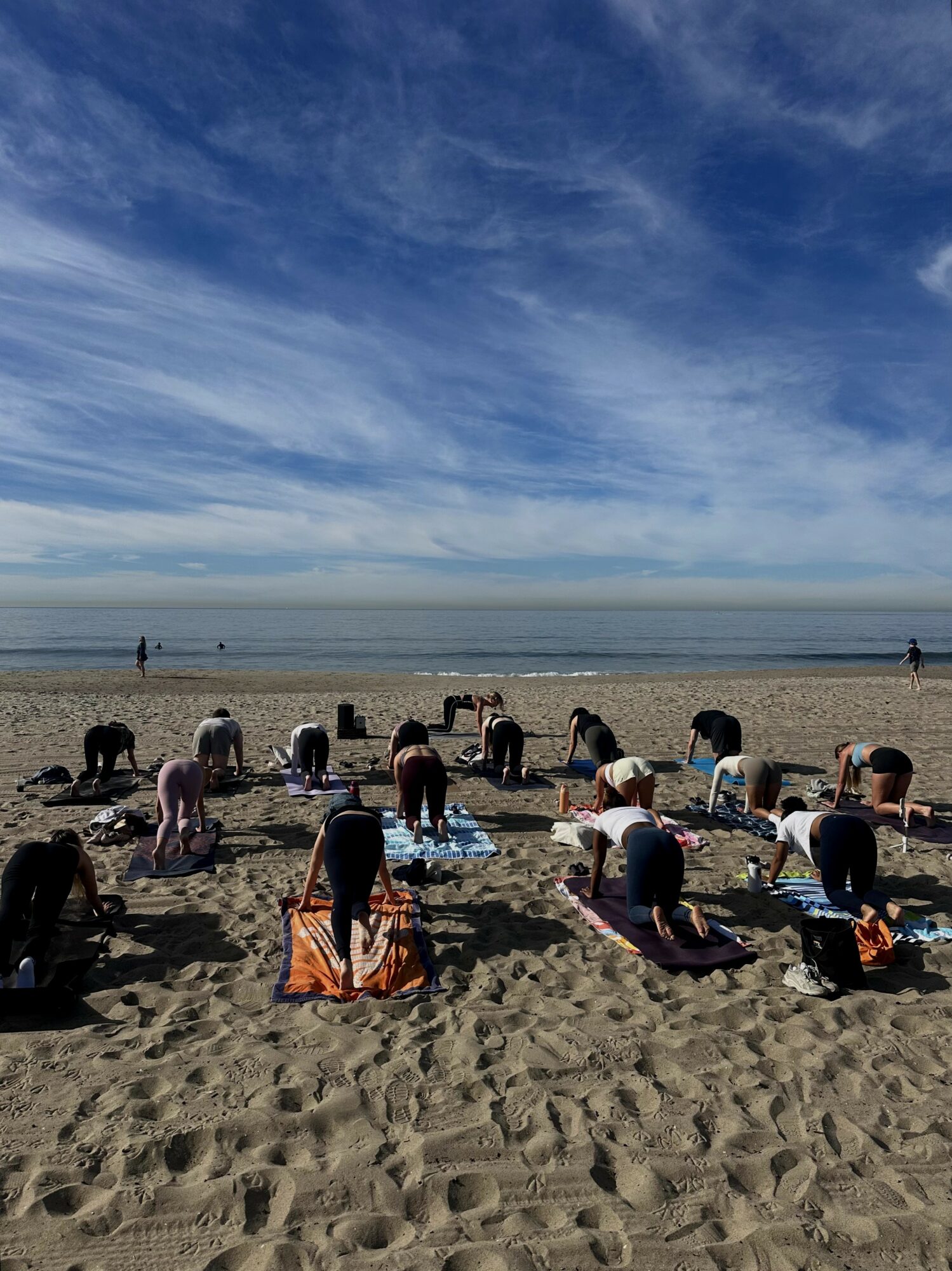 People practicing yoga on a sandy beach with ocean and sky in background.