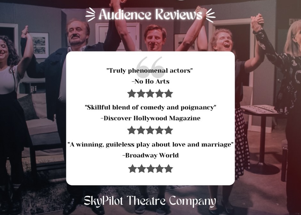 Group of actors on stage celebrating with raised hands, smiling, in a theater setting.