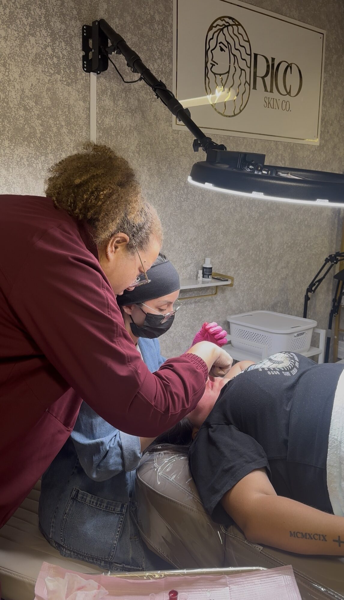 Person lying on dental chair receiving treatment, two dental professionals attending, dental equipment visible.