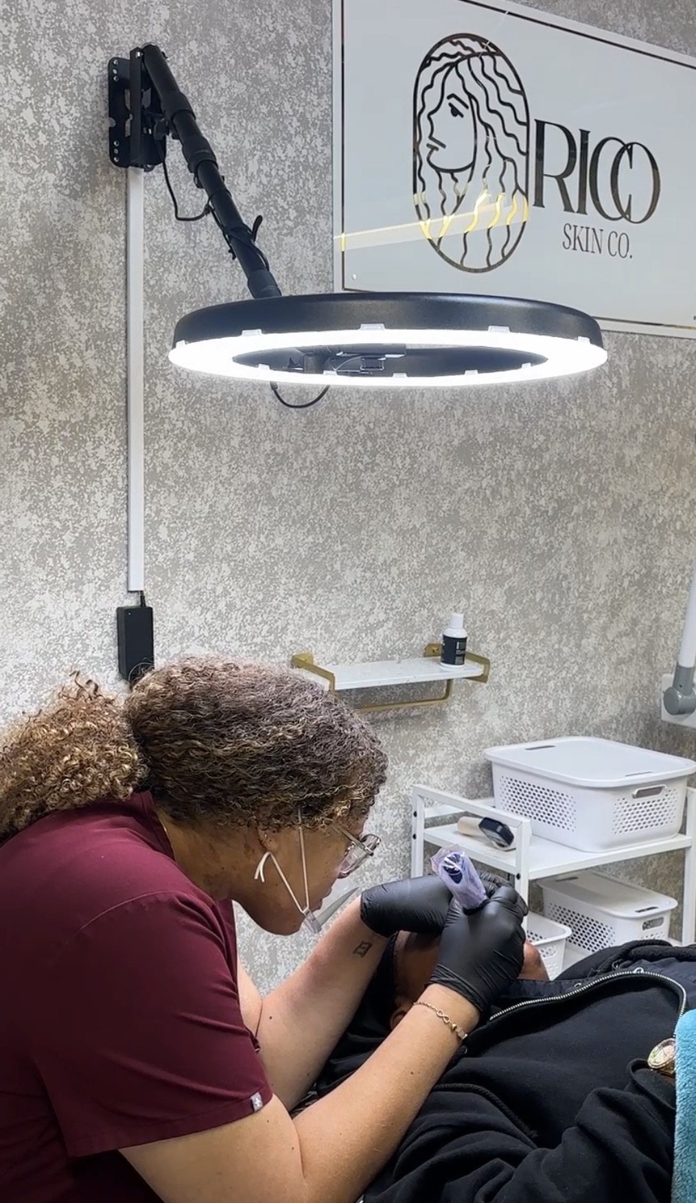 Person working with tools in a workspace, with a ring light overhead and storage containers nearby.