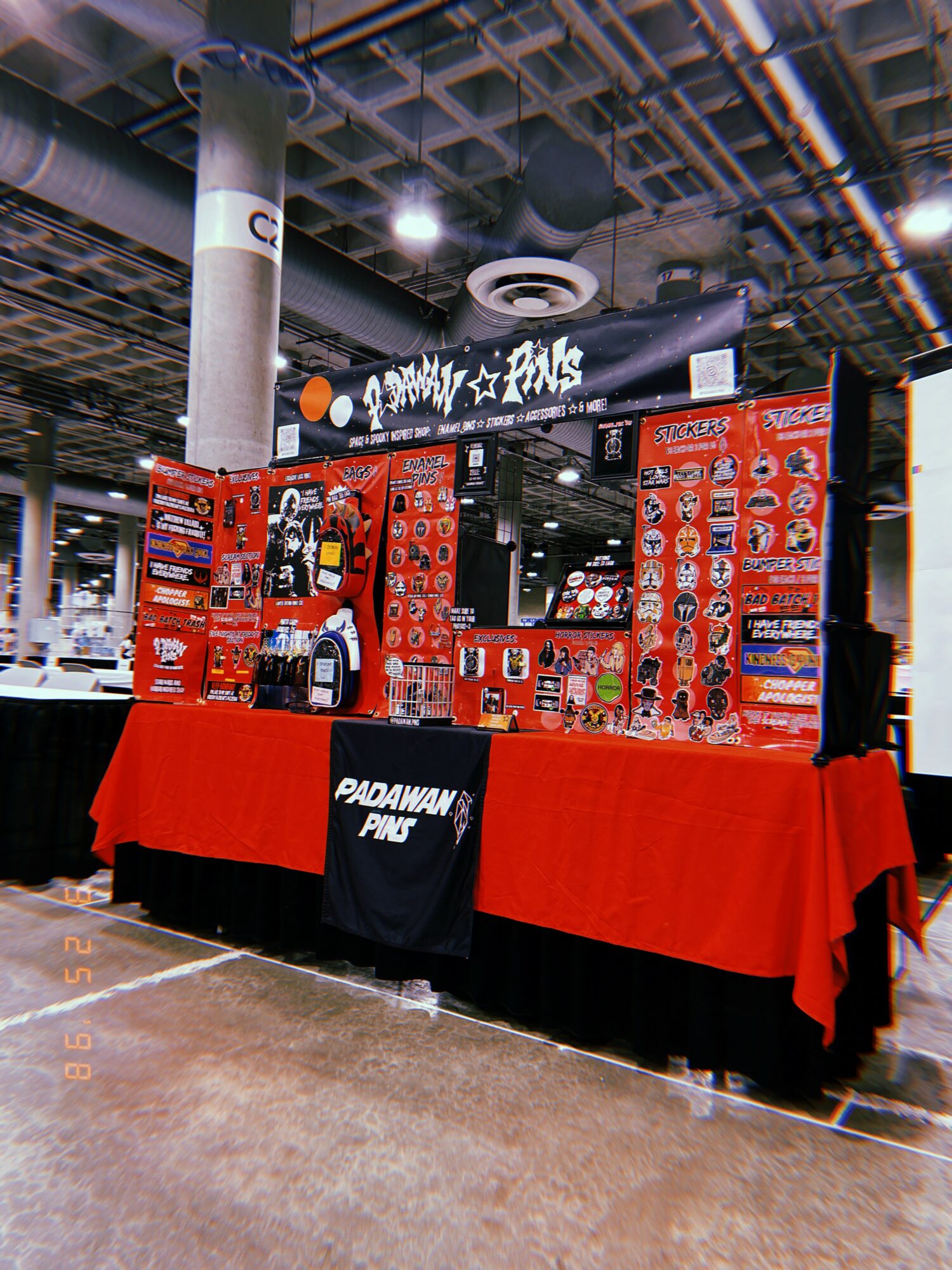 Market stall with red display boards and tablecloth, showcasing various products in an indoor setting.