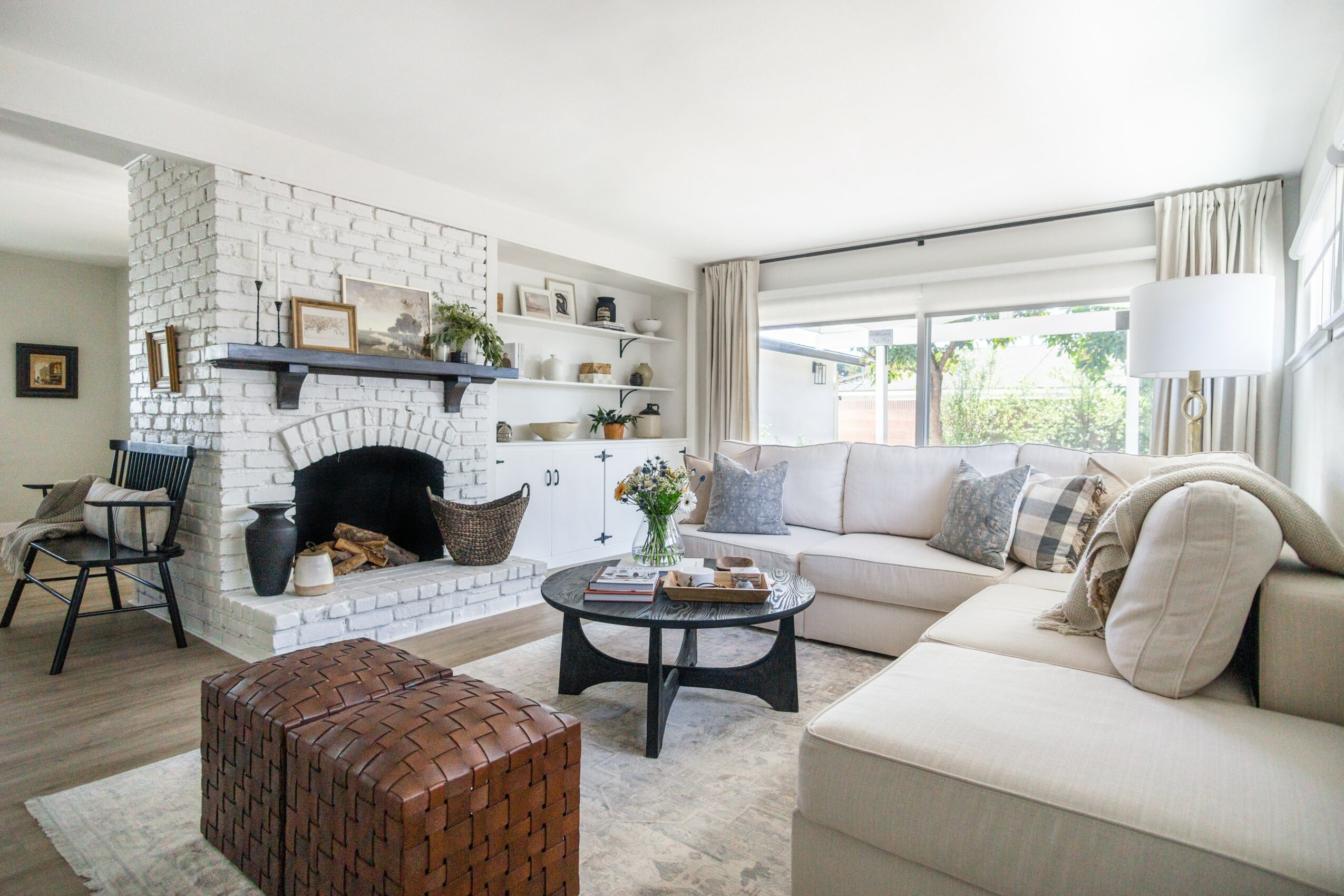 Living room with white brick fireplace, beige sofa, round coffee table, and large window with curtains.