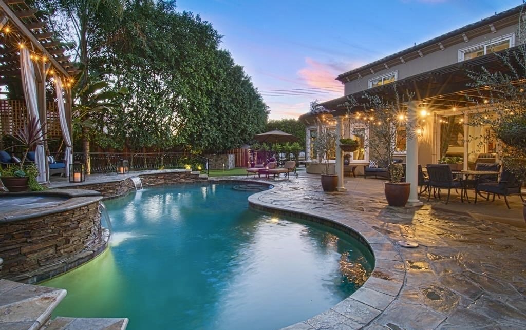 Swimming pool with surrounding patio, trees, and outdoor furniture under evening sky.