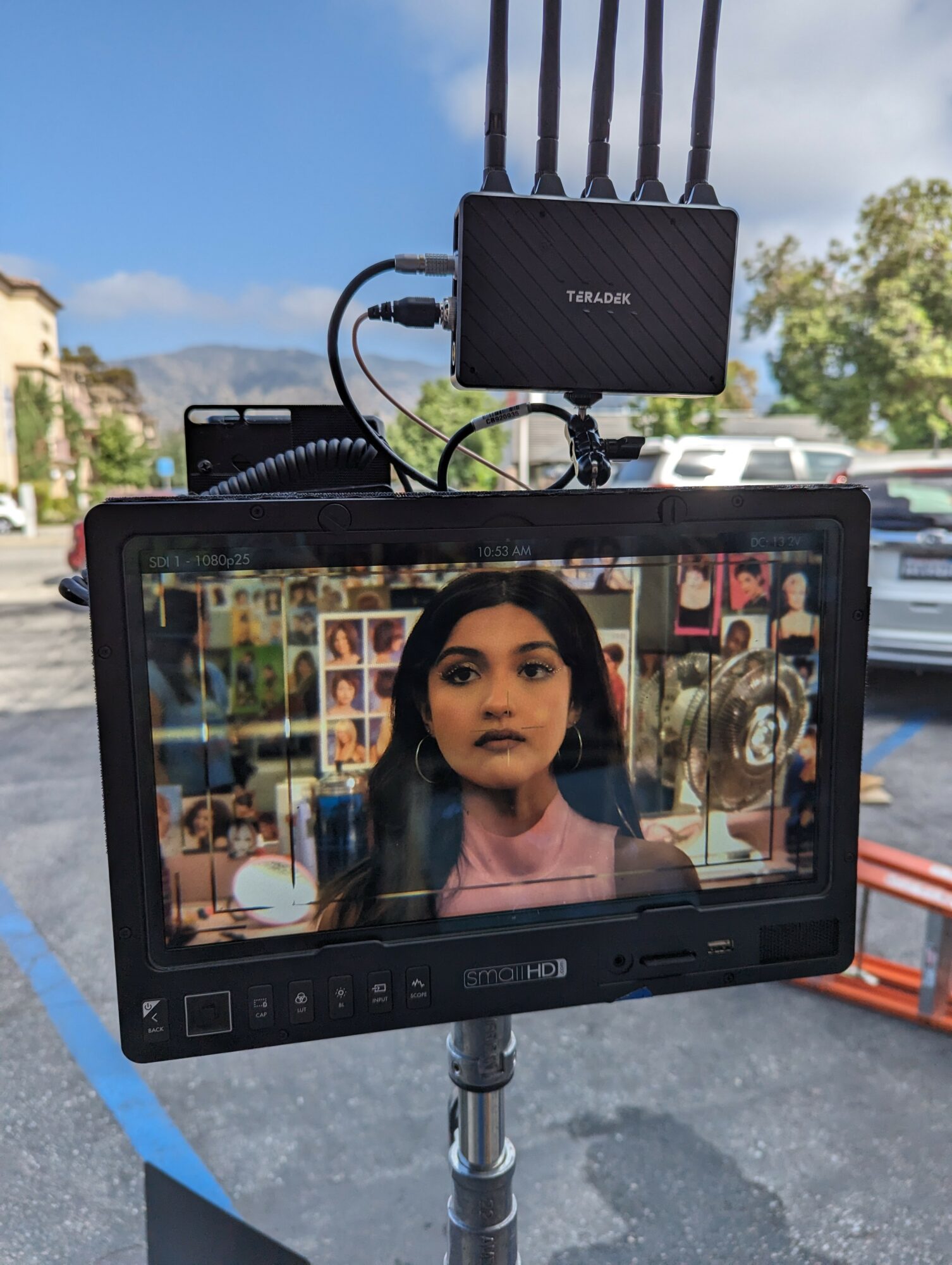 Monitor displaying a woman with dark hair and makeup, in a room with photos and objects in the background.