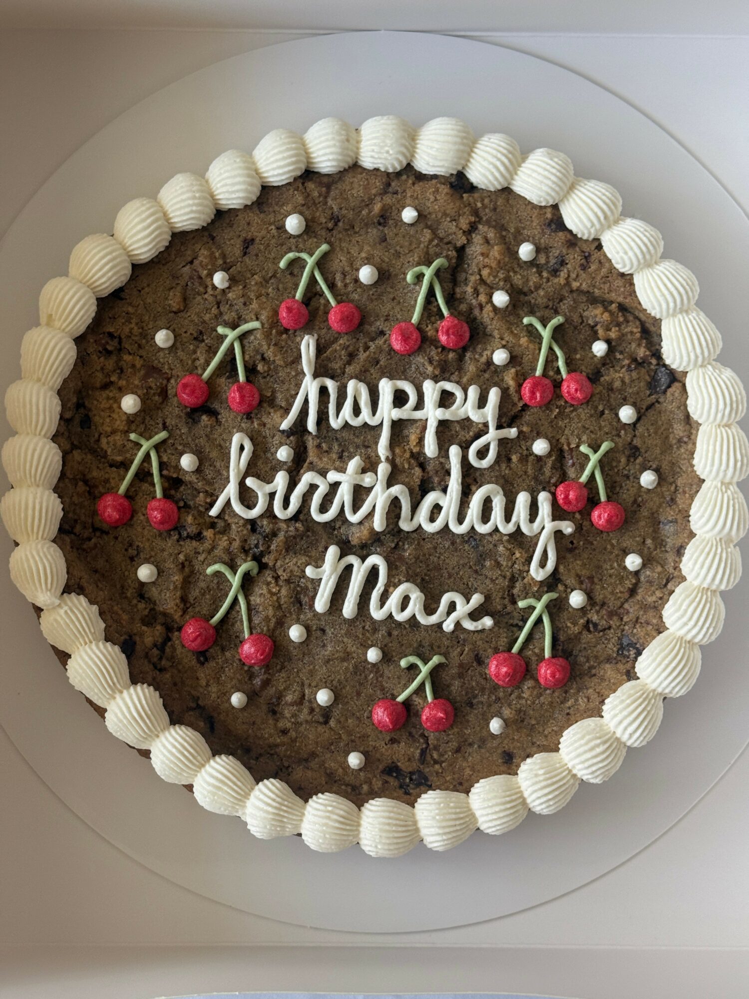 Chocolate birthday cake with white piped border, cherries, and white writing saying 