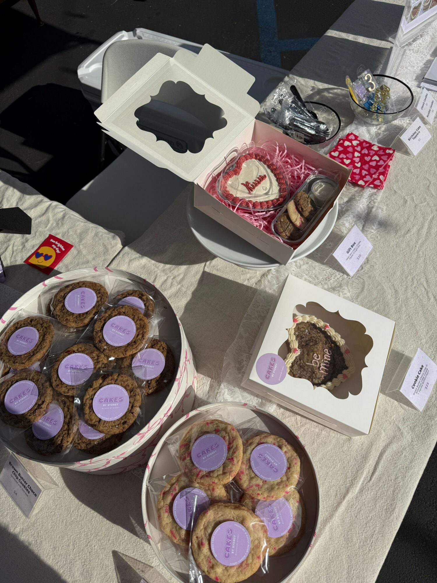 Assorted cookies and baked goods on a table with boxes and labels, some decorated with purple stickers.