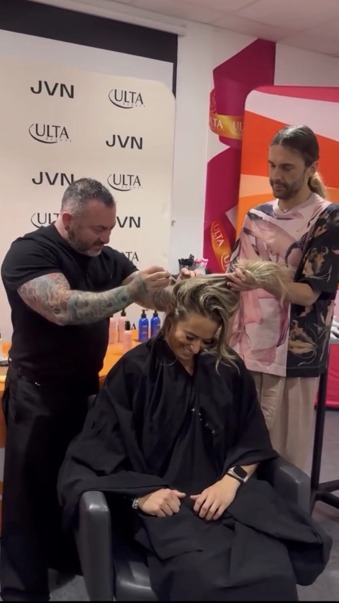 Hairdresser styling woman's hair in salon with colorful background and branded backdrop.