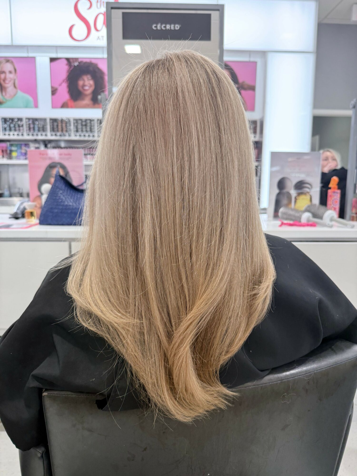 Back of a person's head with long, straight blonde hair in a salon chair.