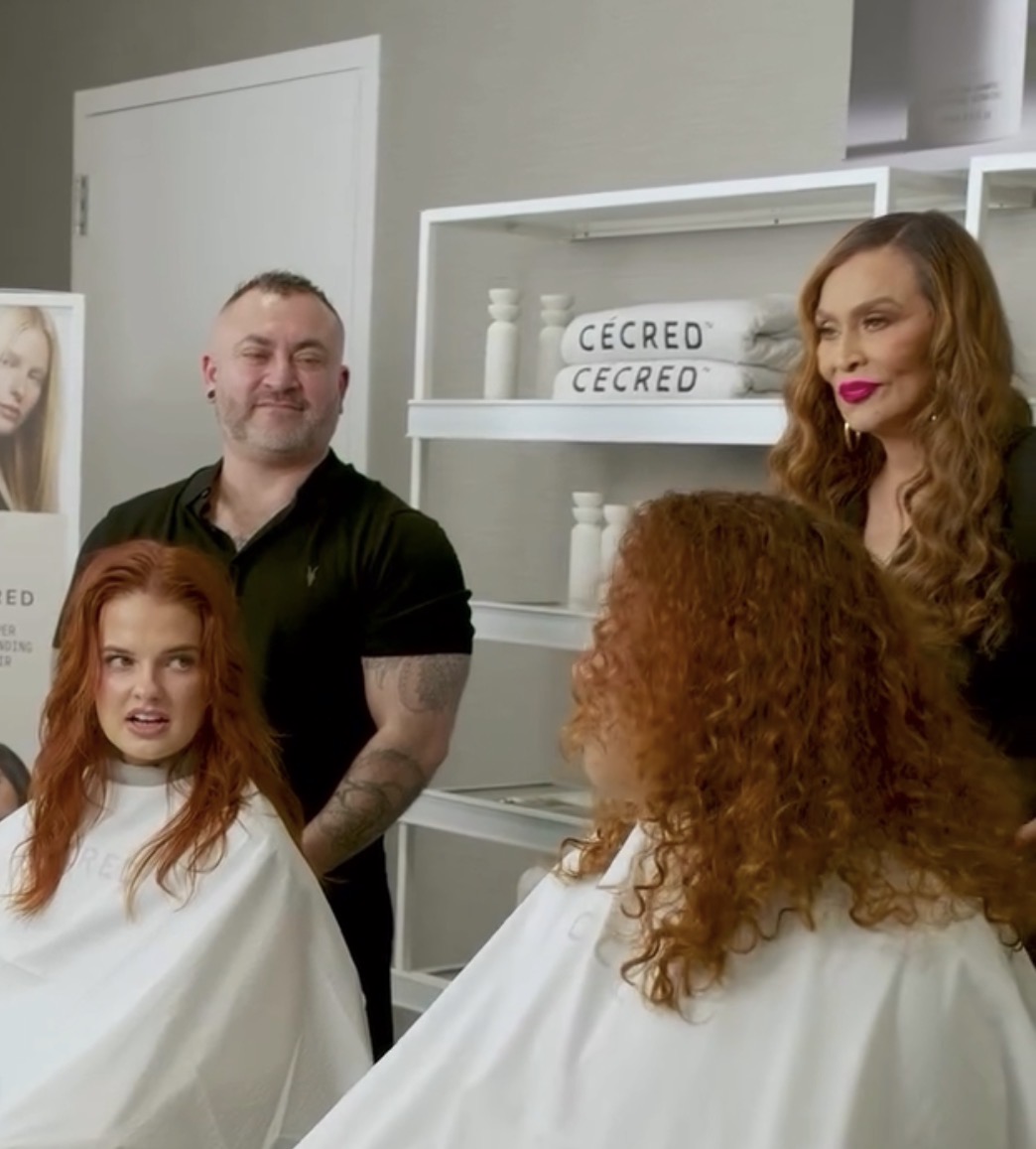 Two women with curly hair and two men in a salon, with shelves and a poster in the background.
