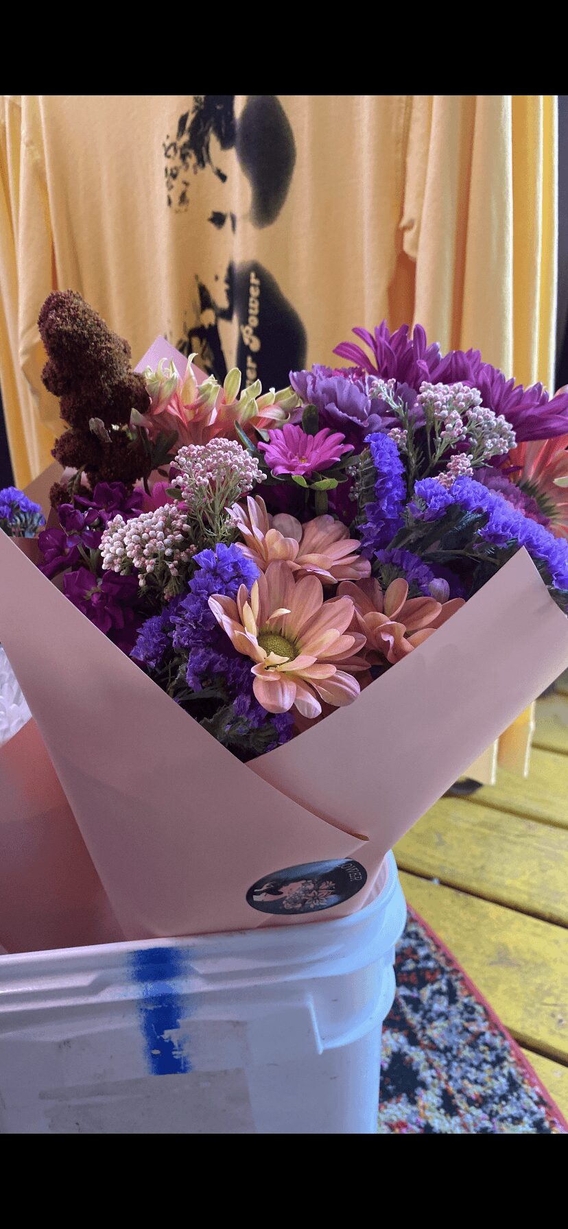 Colorful bouquet of flowers including pink, purple, and white blooms in wrapping paper, placed on a white surface.