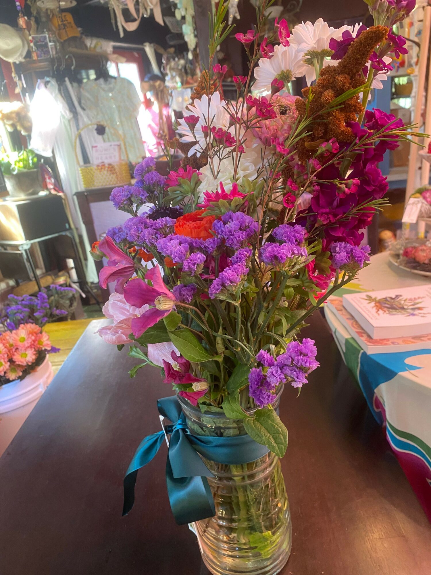 Vase with colorful mixed flowers including pink, purple, and white blooms, tied with a blue ribbon, on a table.