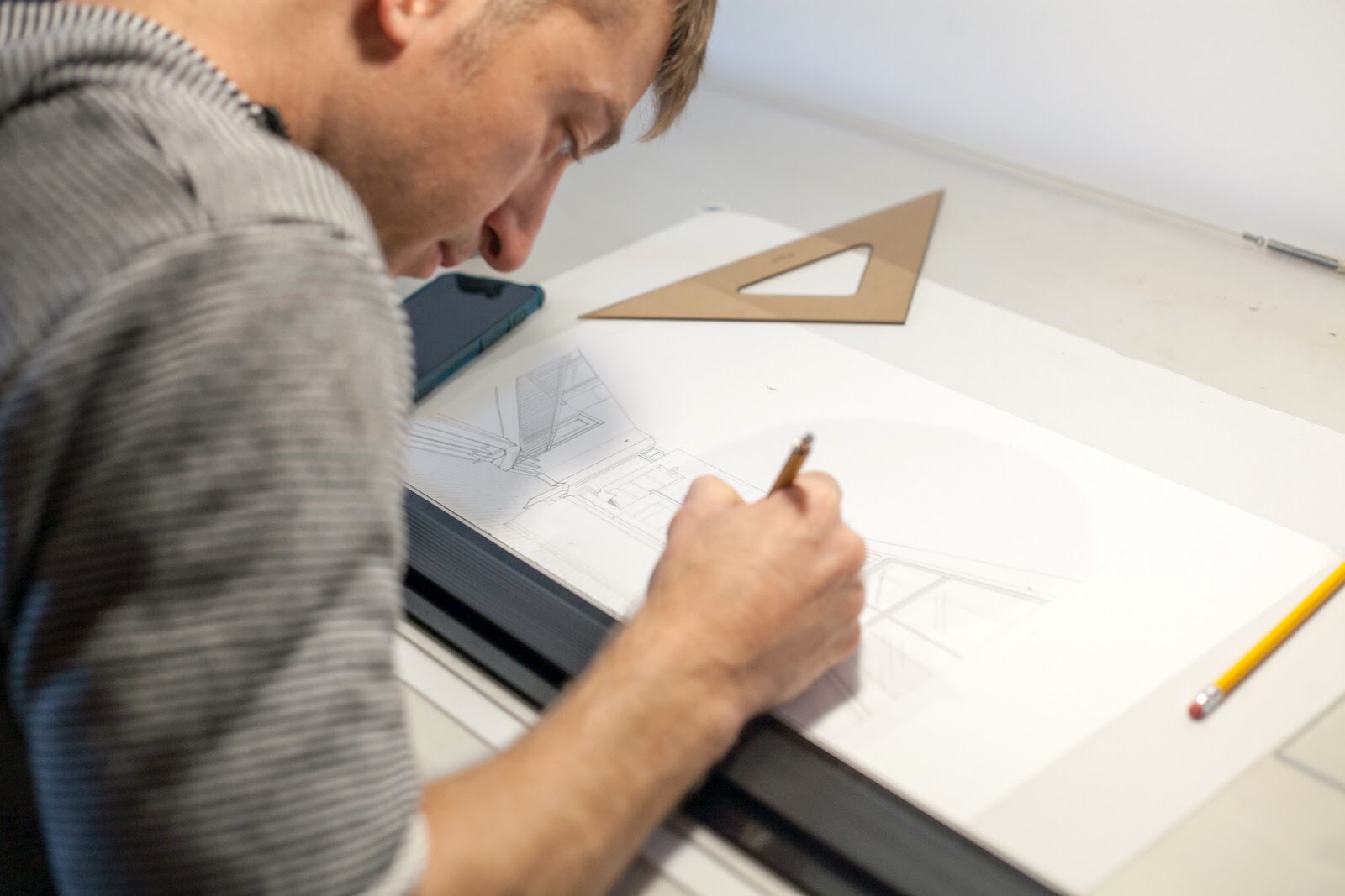 Person drawing on large sheet of paper with a pencil, ruler, and a triangle on the table.