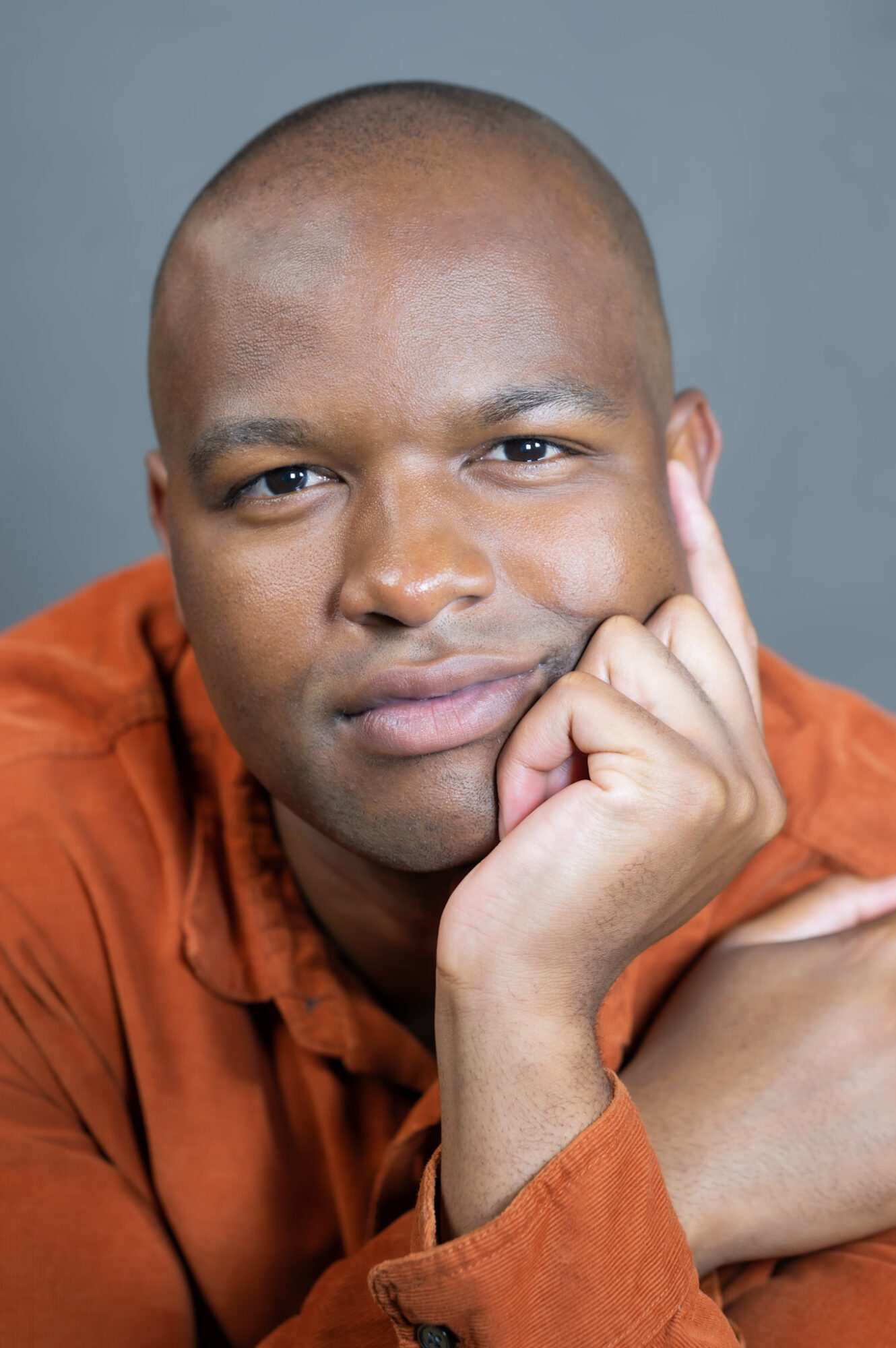 Person with a thoughtful expression, resting their chin on their hand, wearing an orange shirt, against a blue background.