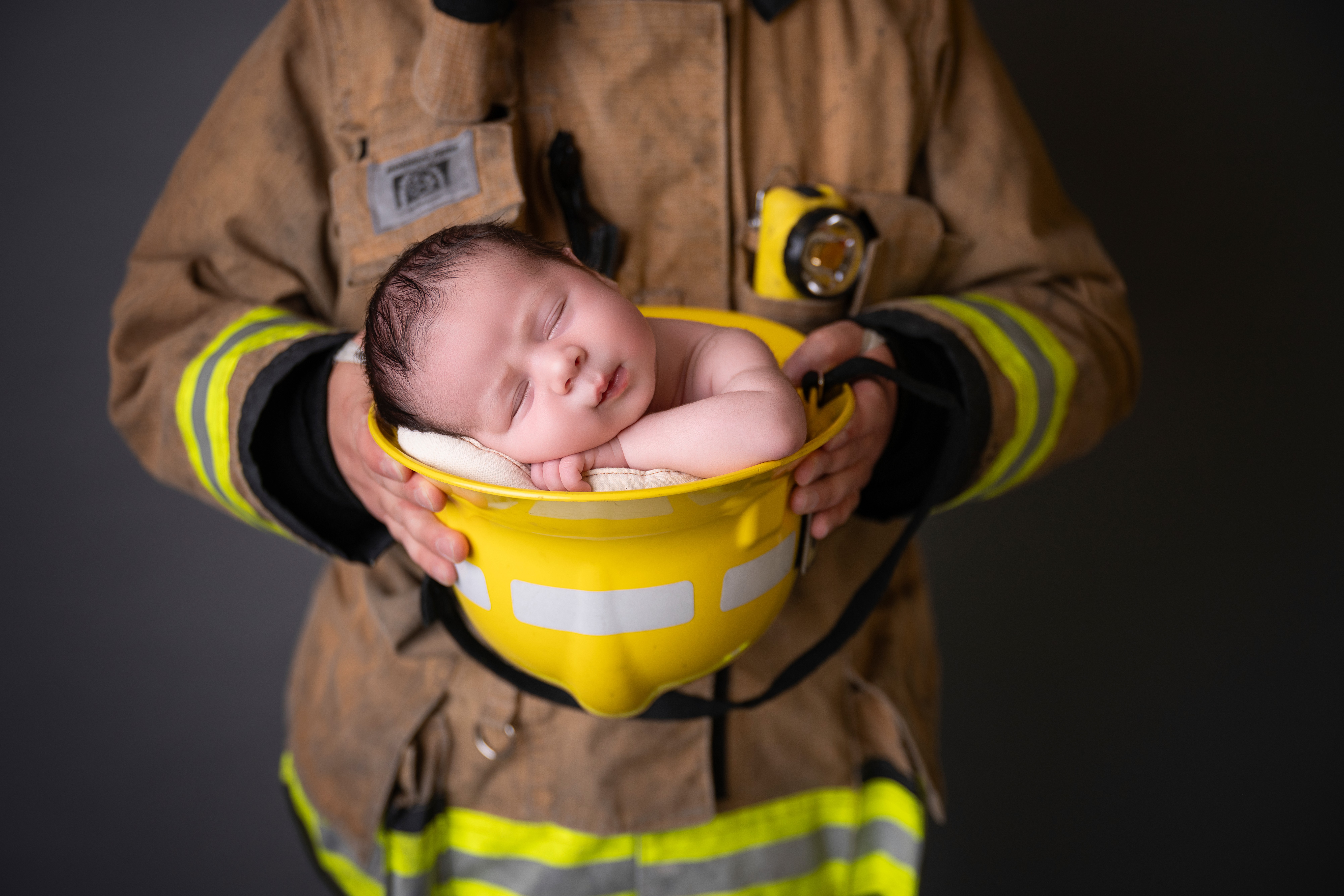 Firefighter holding a yellow bowl with a sleeping baby inside, dark background.