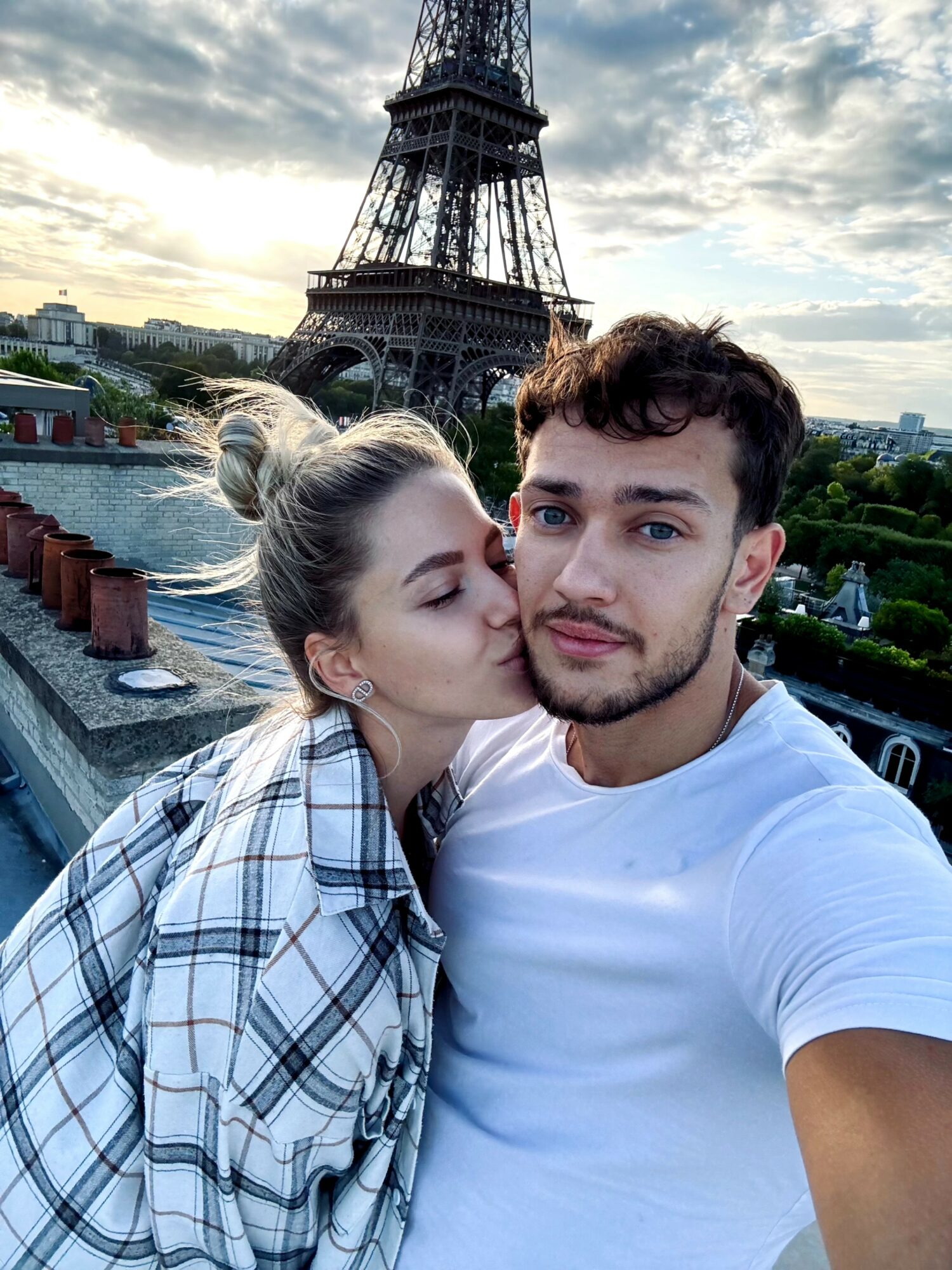 Young woman kisses young man with Eiffel Tower in background during daytime.