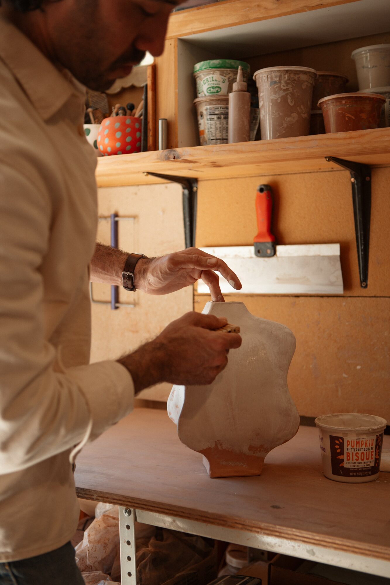 Person working on a ceramic piece in a pottery studio with shelves of clay and tools.