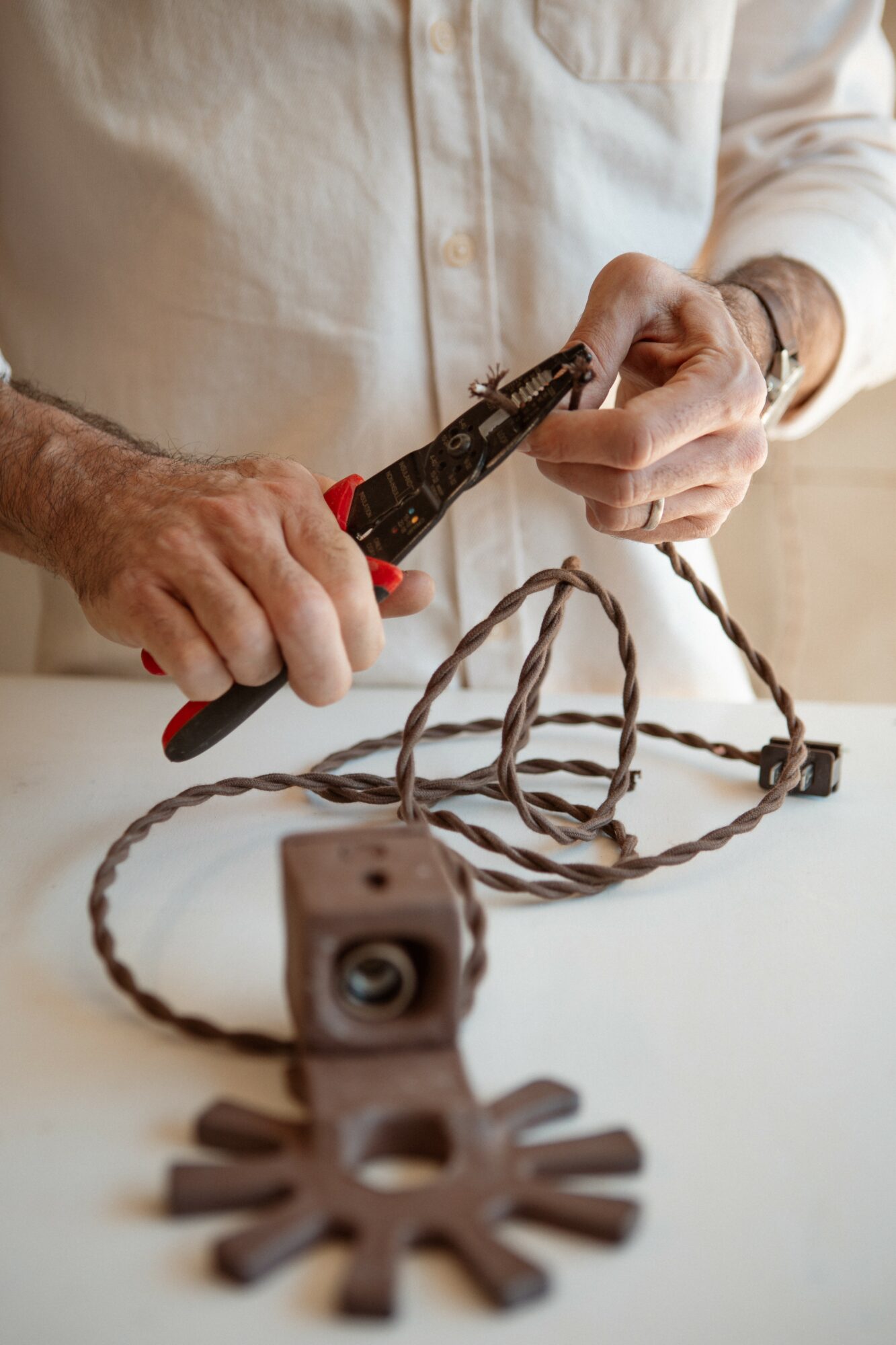 Person using pliers to cut a wire with a gear-shaped object and a camera on a white surface.