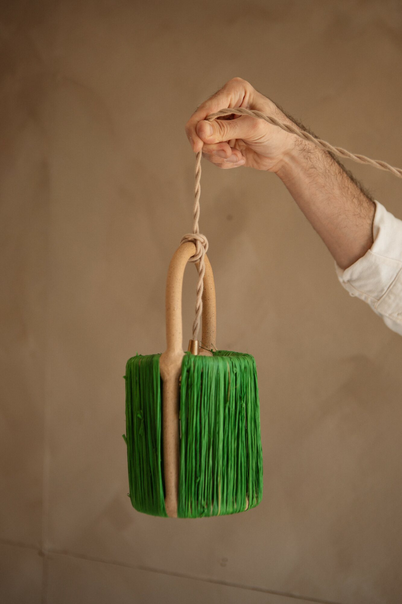 Hand holding a broom with a green bristle head and a wooden handle, suspended by a rope.