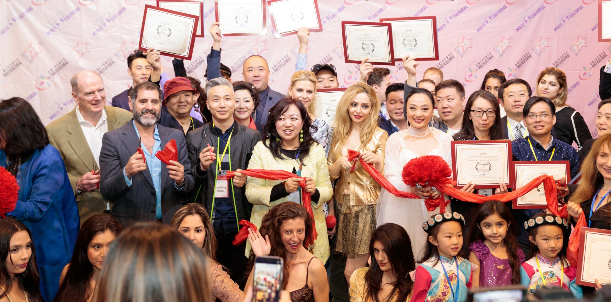 Group of people holding certificates and a large red ribbon at an event, smiling and celebrating.