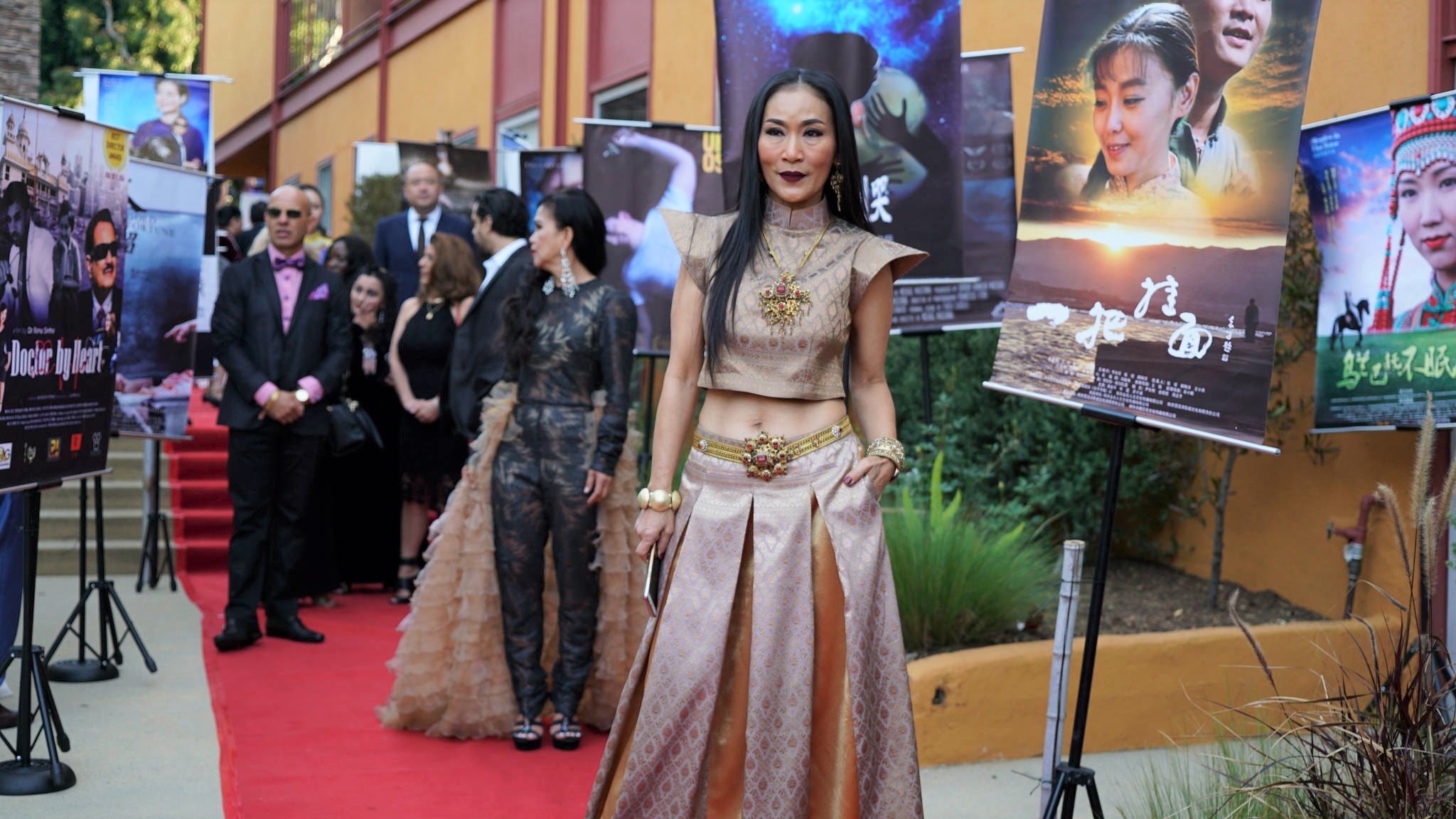 Group of people at an event with posters and a red carpet, woman in traditional attire in foreground.