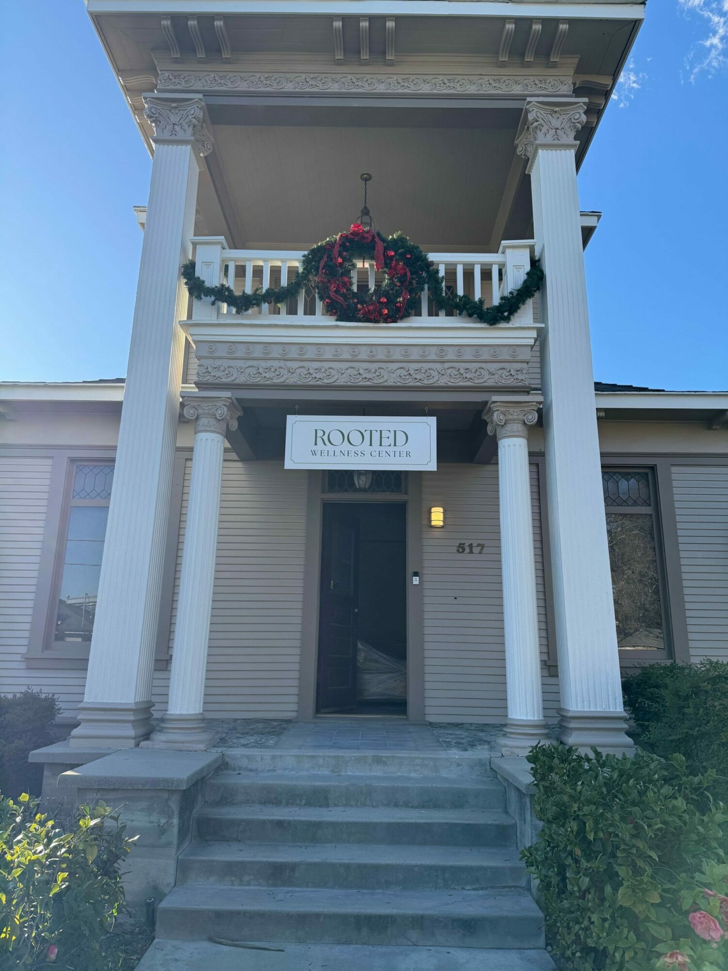 Front porch with stairs, white columns, and a hanging flower basket, leading to a building with a sign reading 'LUXE'.