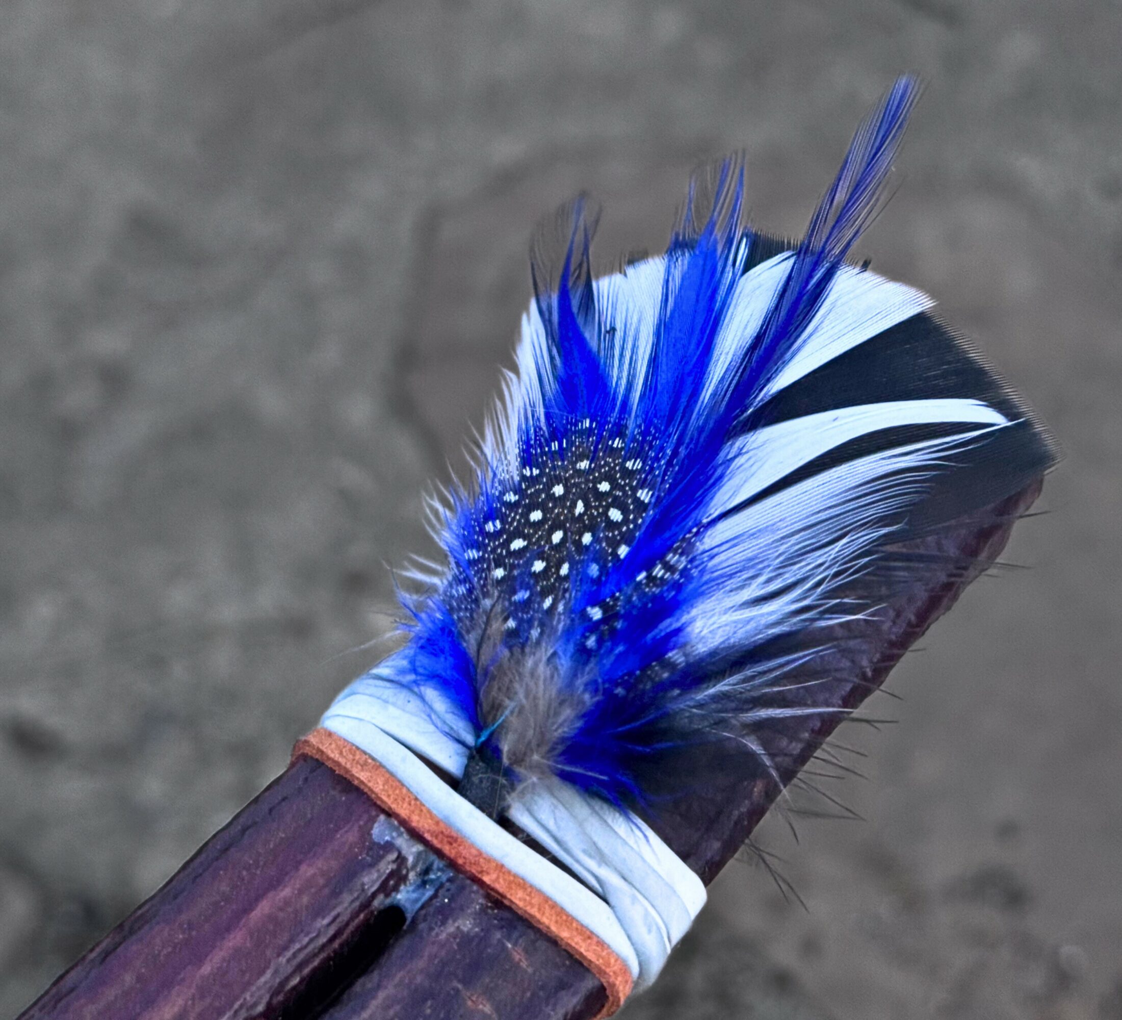 Close-up of a decorated stick with blue, white, and black feathers and small white dots.