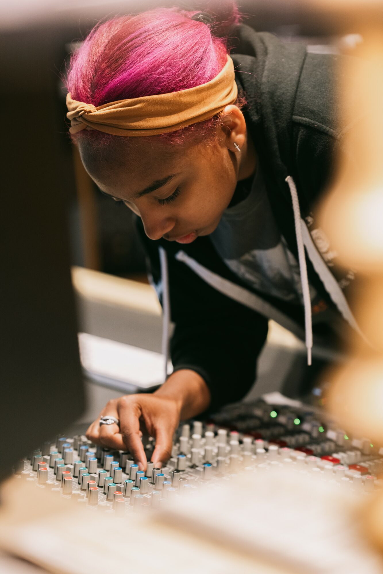 Person with pink hair adjusting sound equipment in a dimly lit environment.