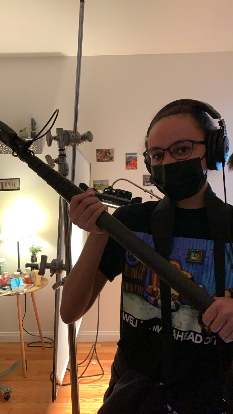 Person wearing glasses and a face mask holding a large camera or equipment indoors.