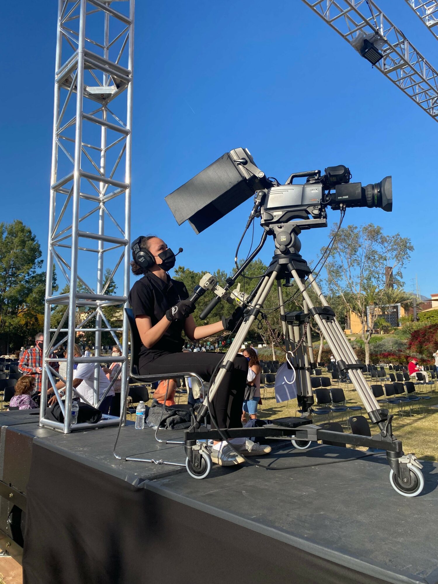 Person operating a large professional camera on a mobile tripod outdoors during daytime.
