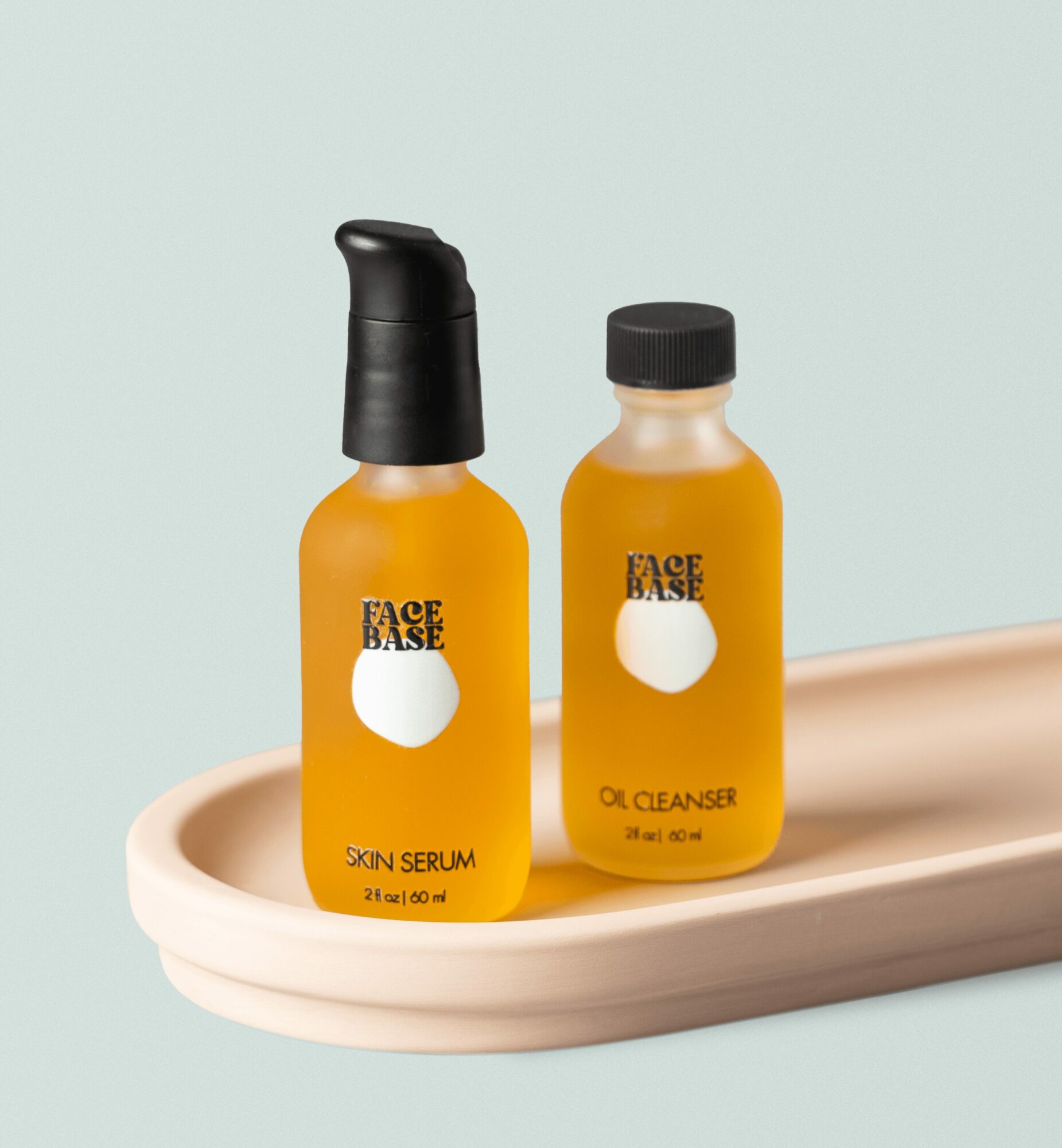 Two small yellow bottles labeled face base, one with a pump and the other with a screw cap, on a beige dish.